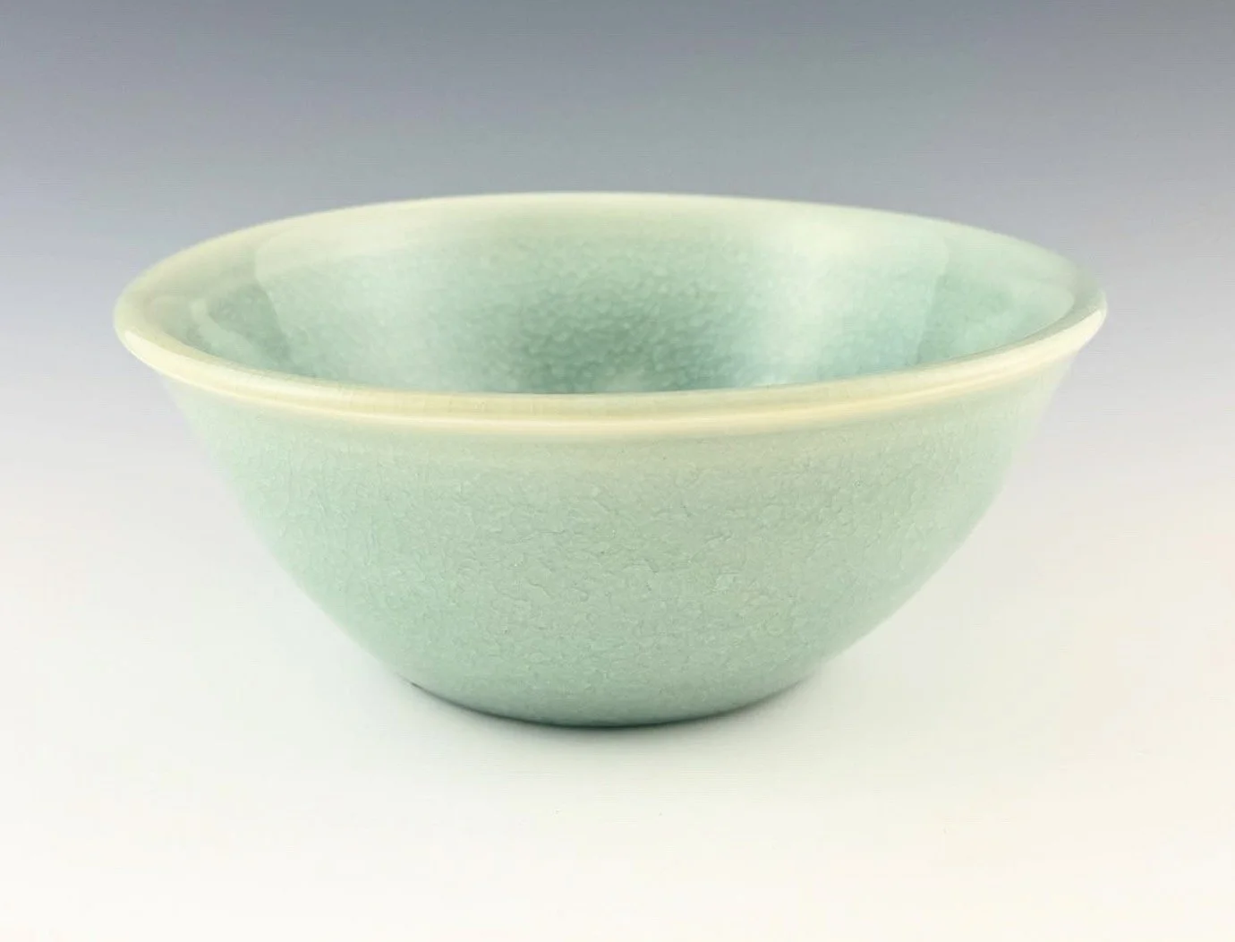 Pale aquamarine porcelain bowl with a celadon glaze on a plain white background.