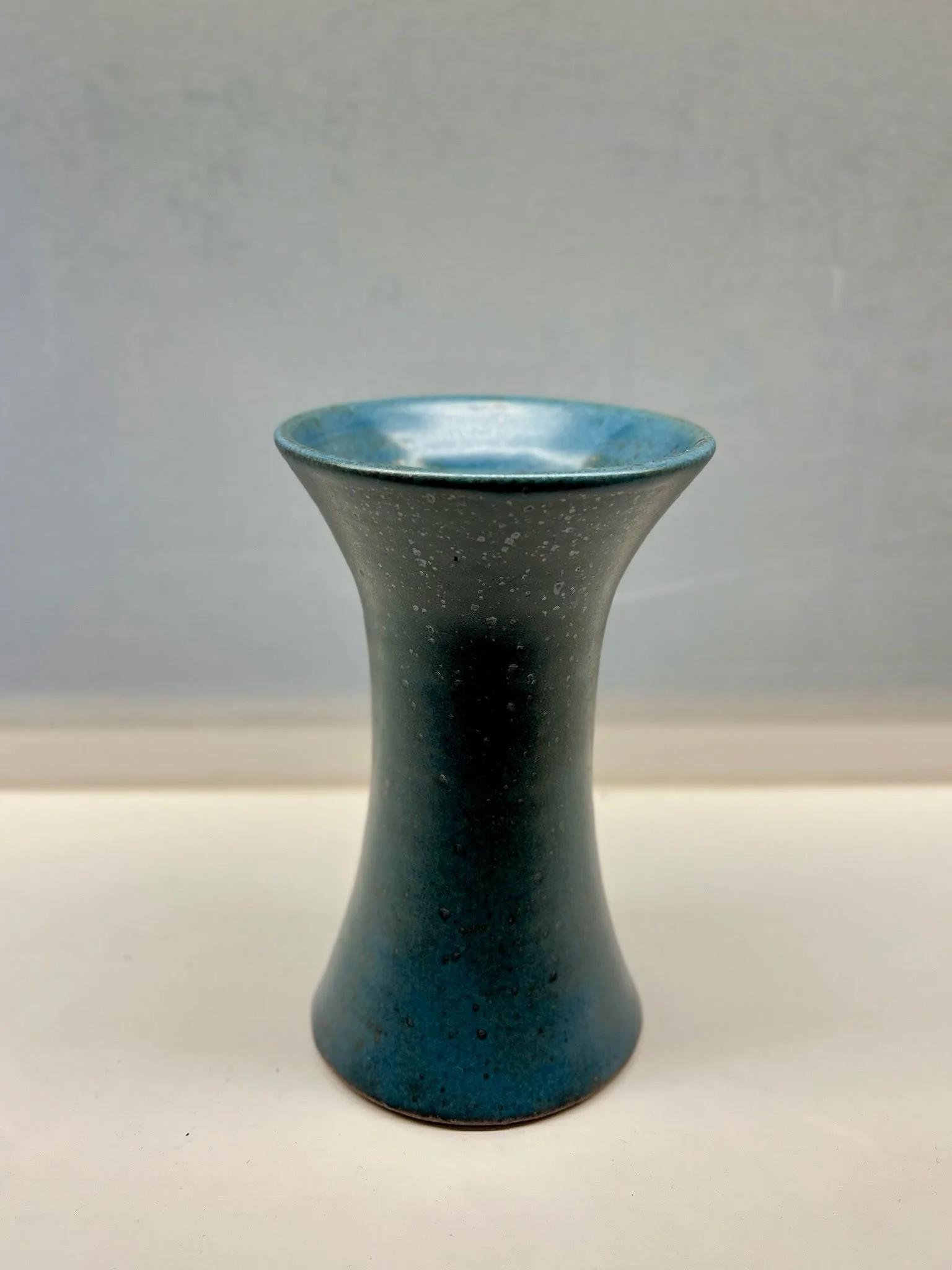 A ceramic vase with a blue interior and a dark exterior, shaped like an hourglass.