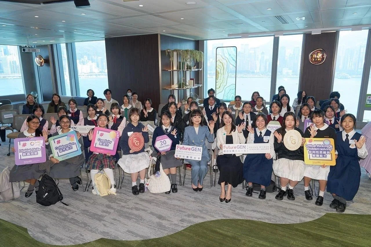 Group of young women in school uniforms sitting and standing in a modern room with large windows, holding signs related to future generation and women's empowerment.
