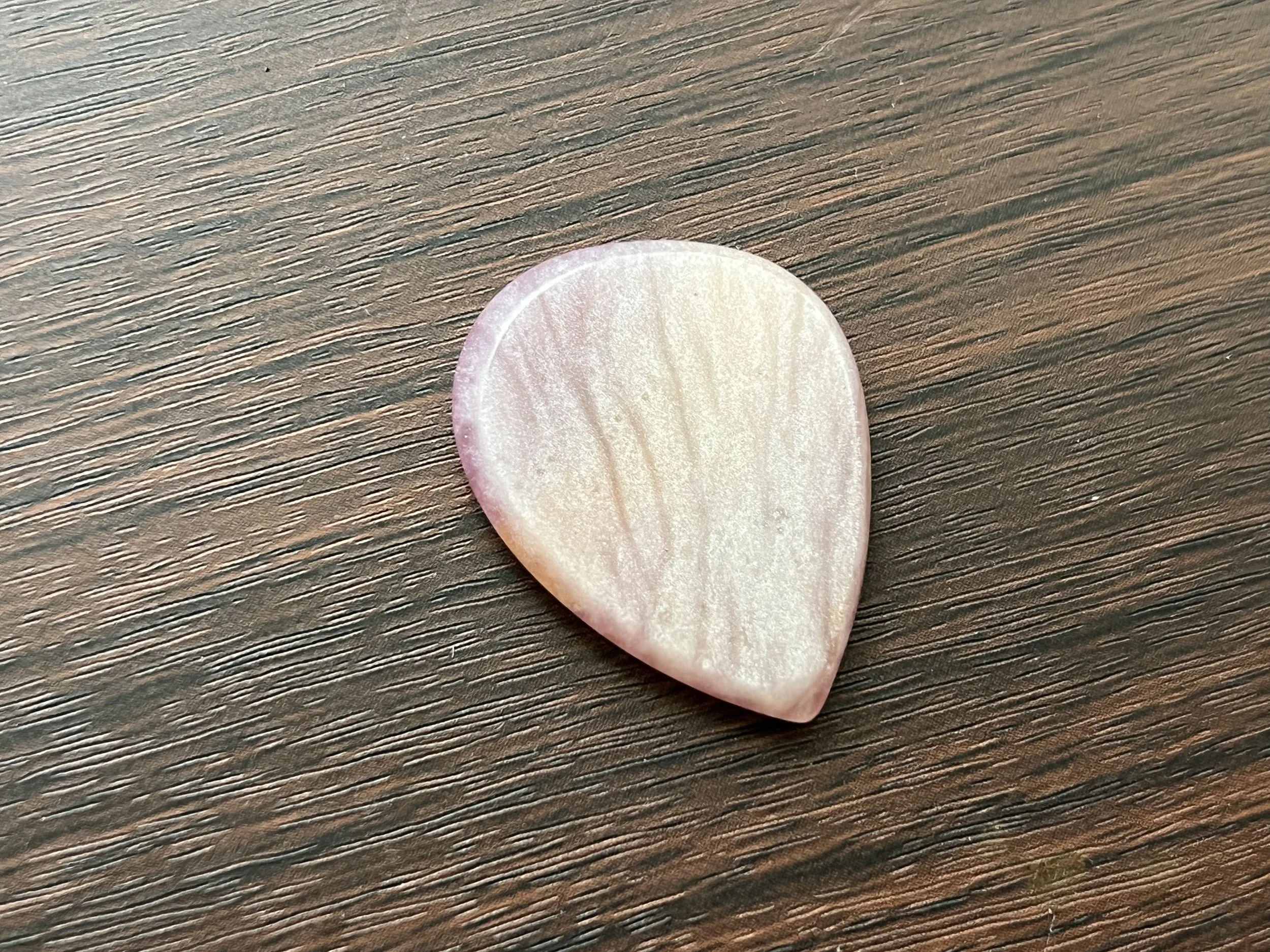A pink and white striped heart-shaped object resting on a dark brown wooden surface.