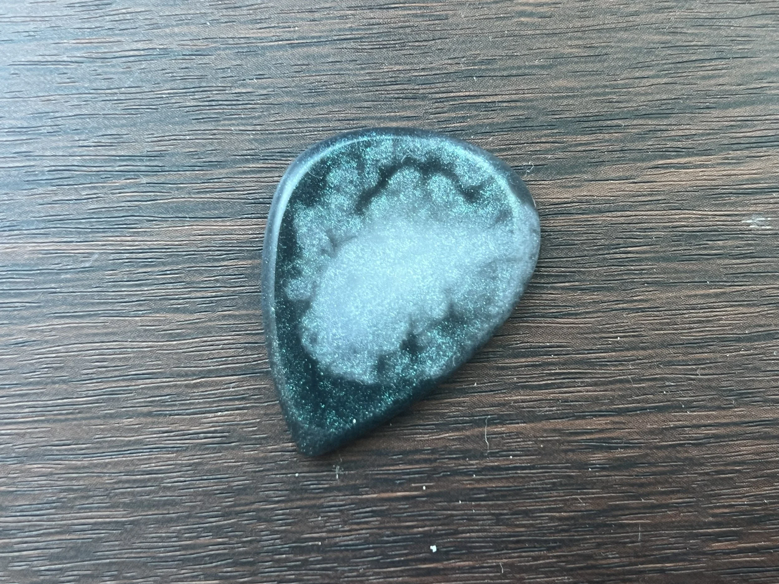 A translucent blue-green gummy candy shaped like a football, sitting on a wooden surface.