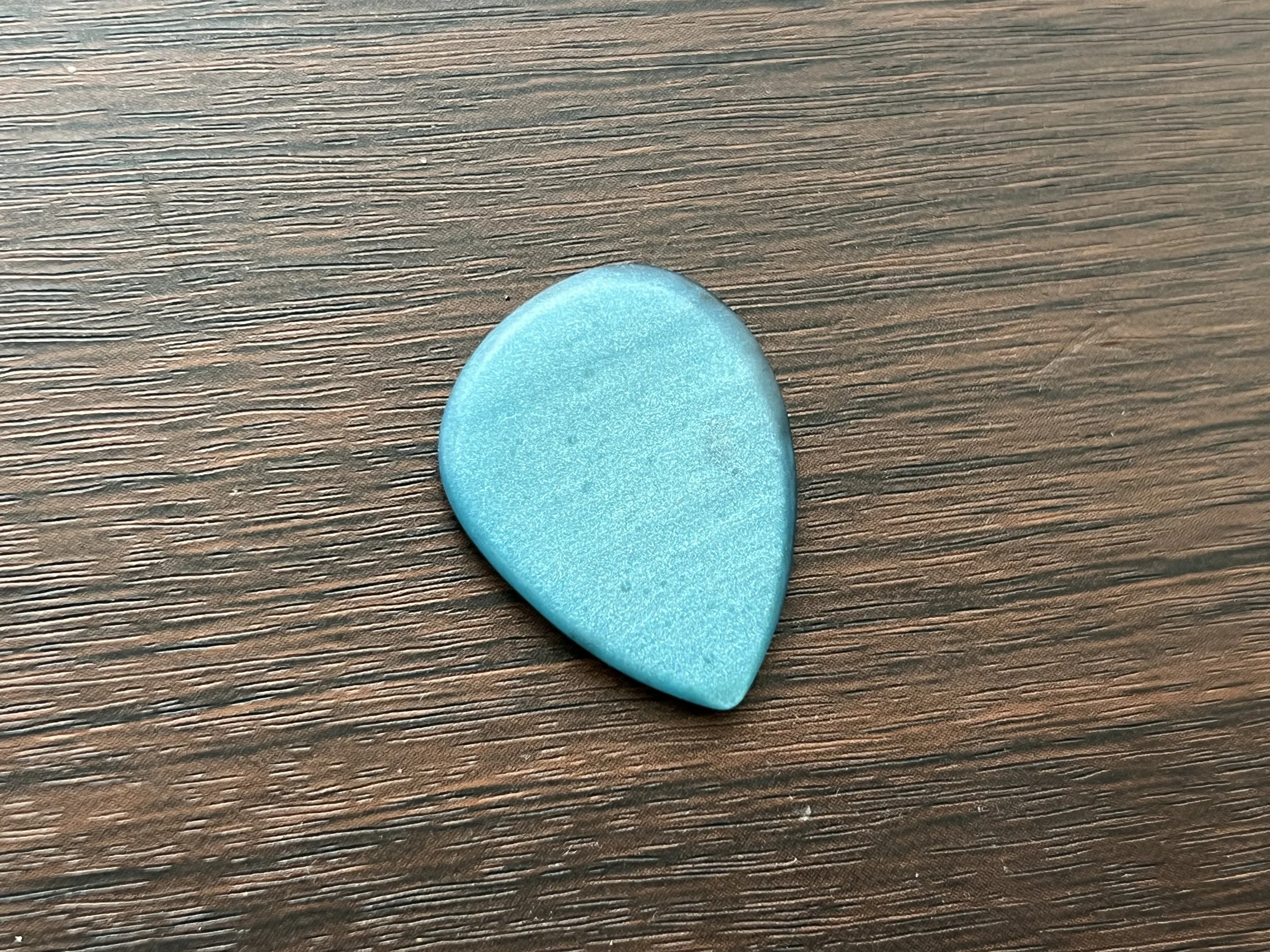 A smooth, blue, heart-shaped object on a textured dark brown wooden surface.