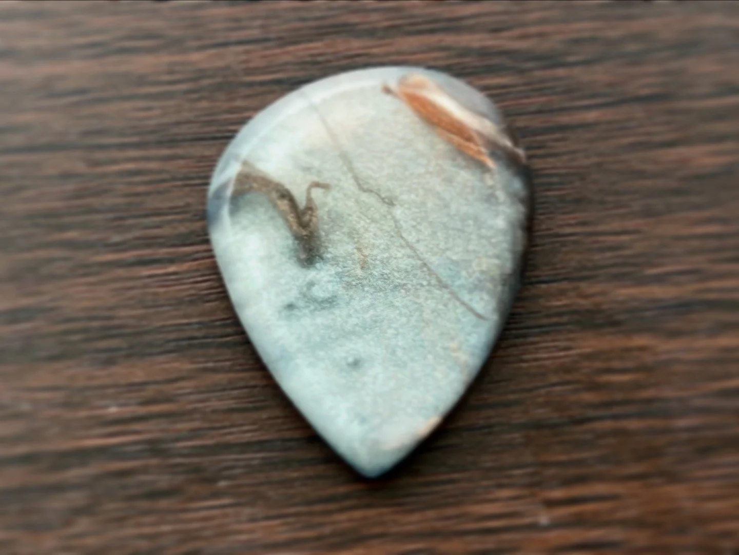 A guitar pick with a cloudy, marble-like pattern on a wooden surface.