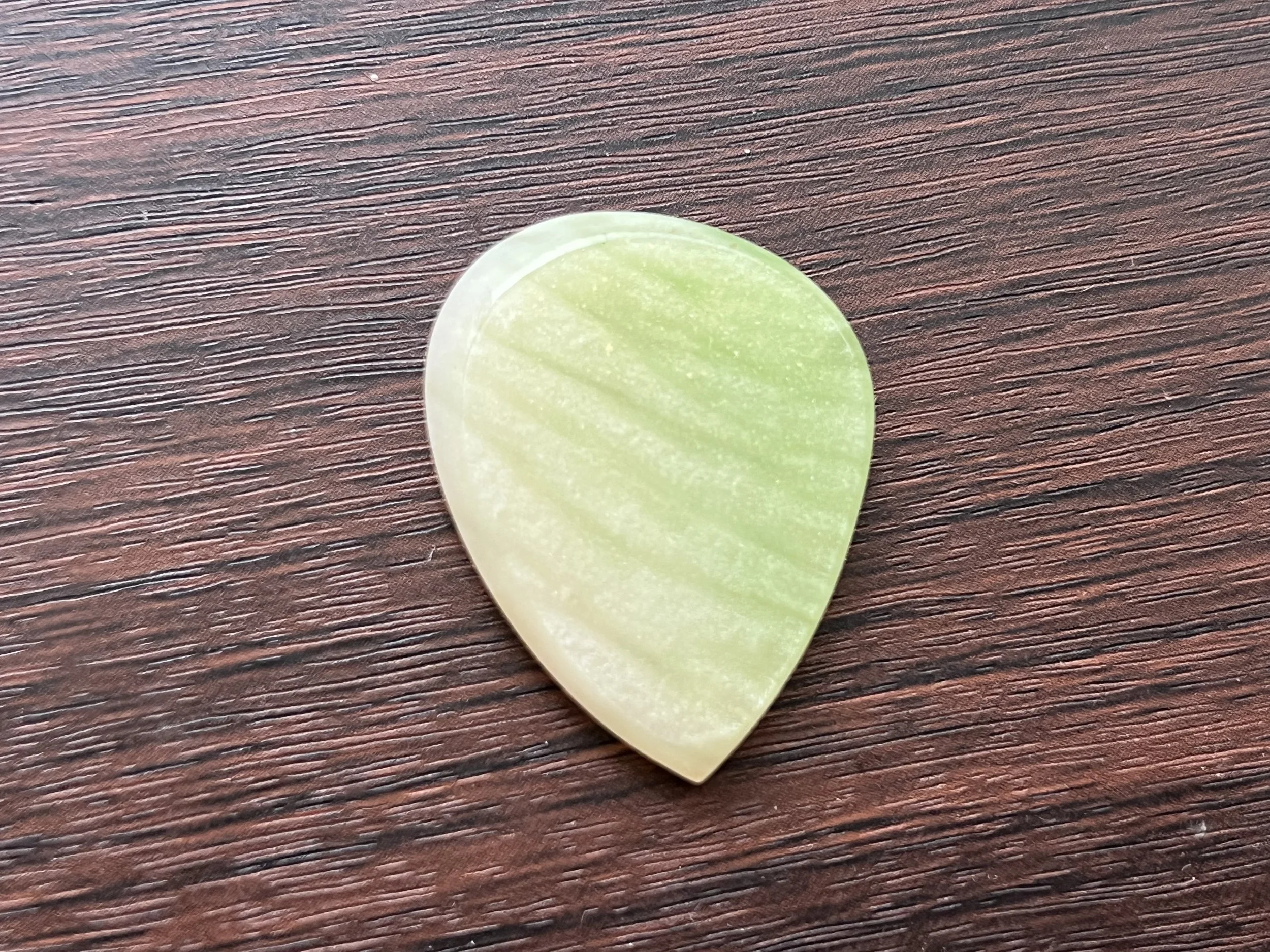A close-up of a green guitar pick resting on a wooden surface.