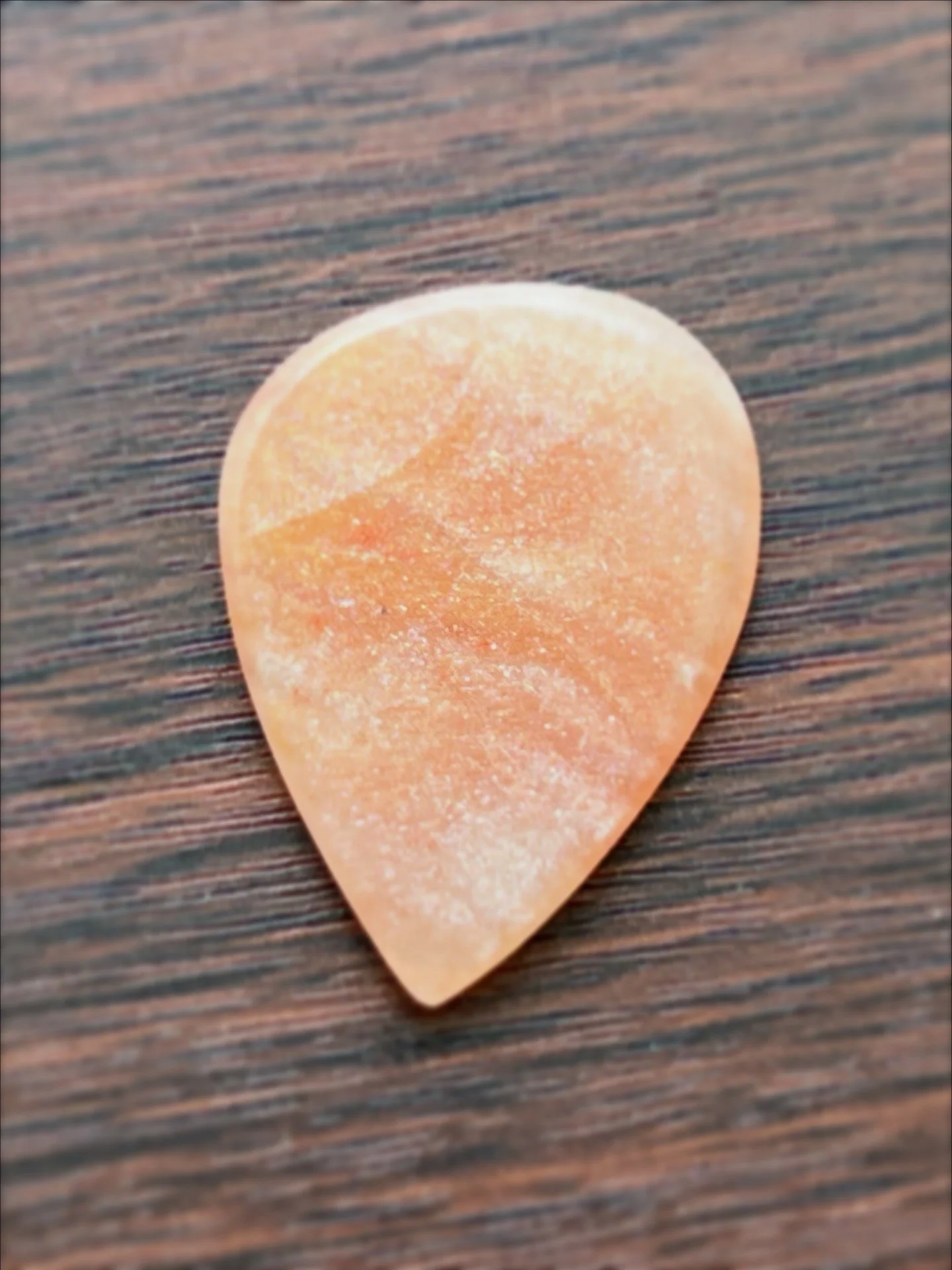 A close-up of a peach-colored guitar pick on a dark wooden surface.
