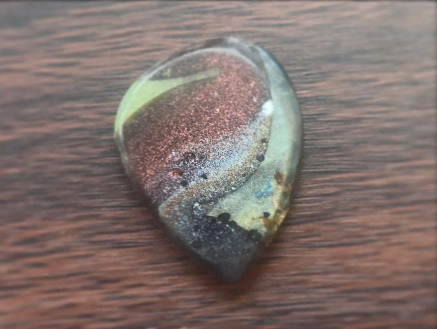 Close-up of a small, smooth stone with multicolored patterns and textures, resting on a dark wooden surface.