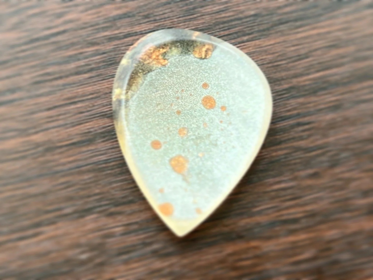 Close-up image of a guitar pick with a translucent surface and orange spots on a wooden surface.