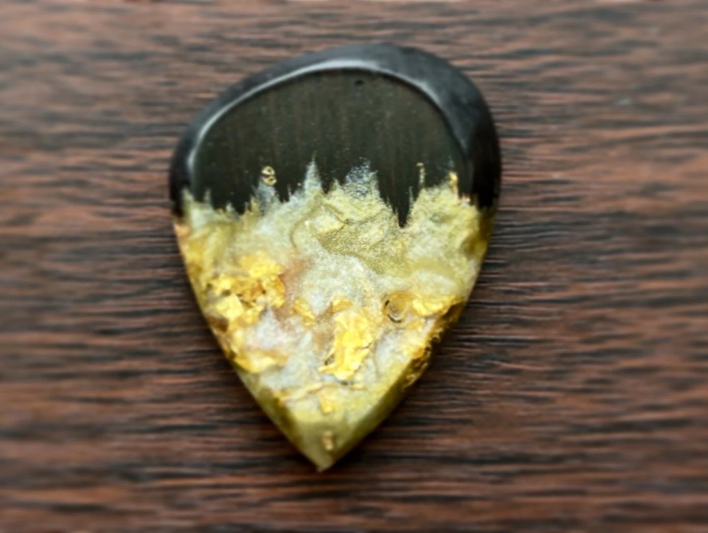 A guitar pick with a black and yellow design, placed on a wooden surface.