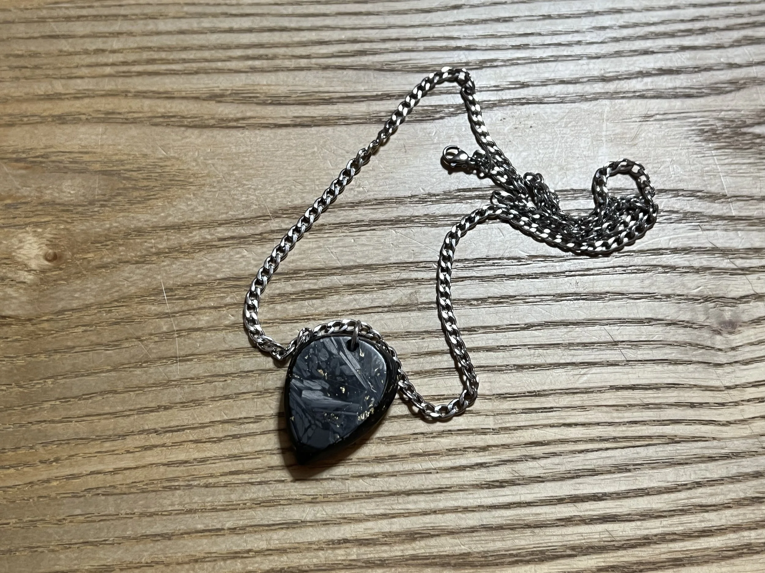 A black heart-shaped pendant with a shiny, cracked surface, hanging from a silver chain on a wooden surface.