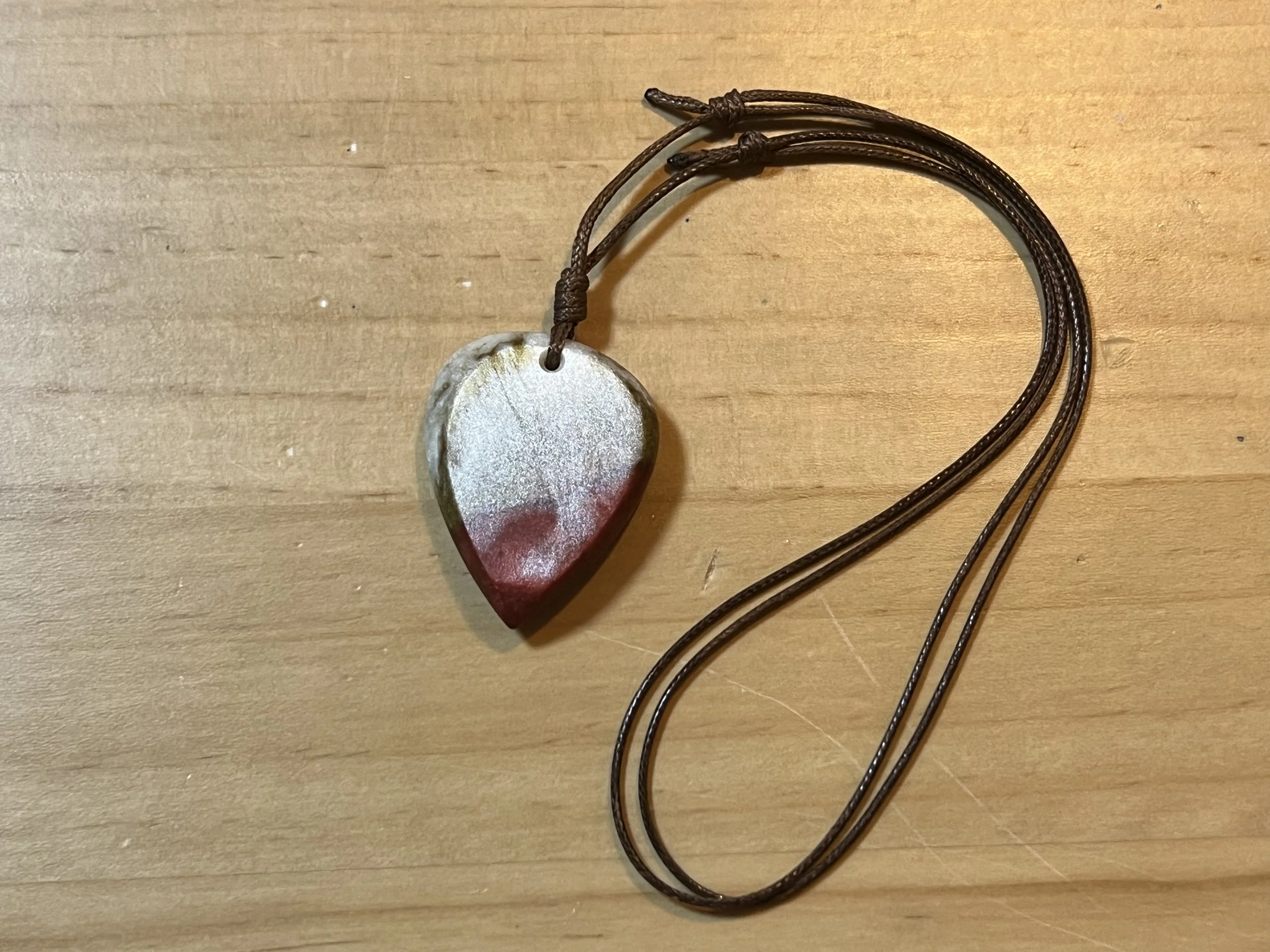 Heart-shaped stone pendant on a brown cord necklace resting on a wooden surface.