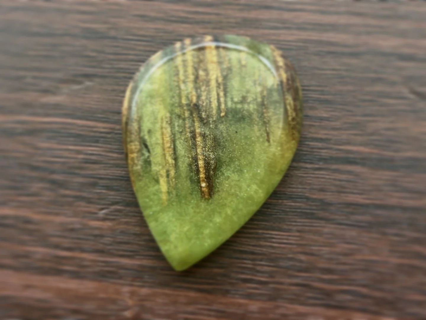 Close-up of a green gemstone with black and yellow streaks on a wooden surface.