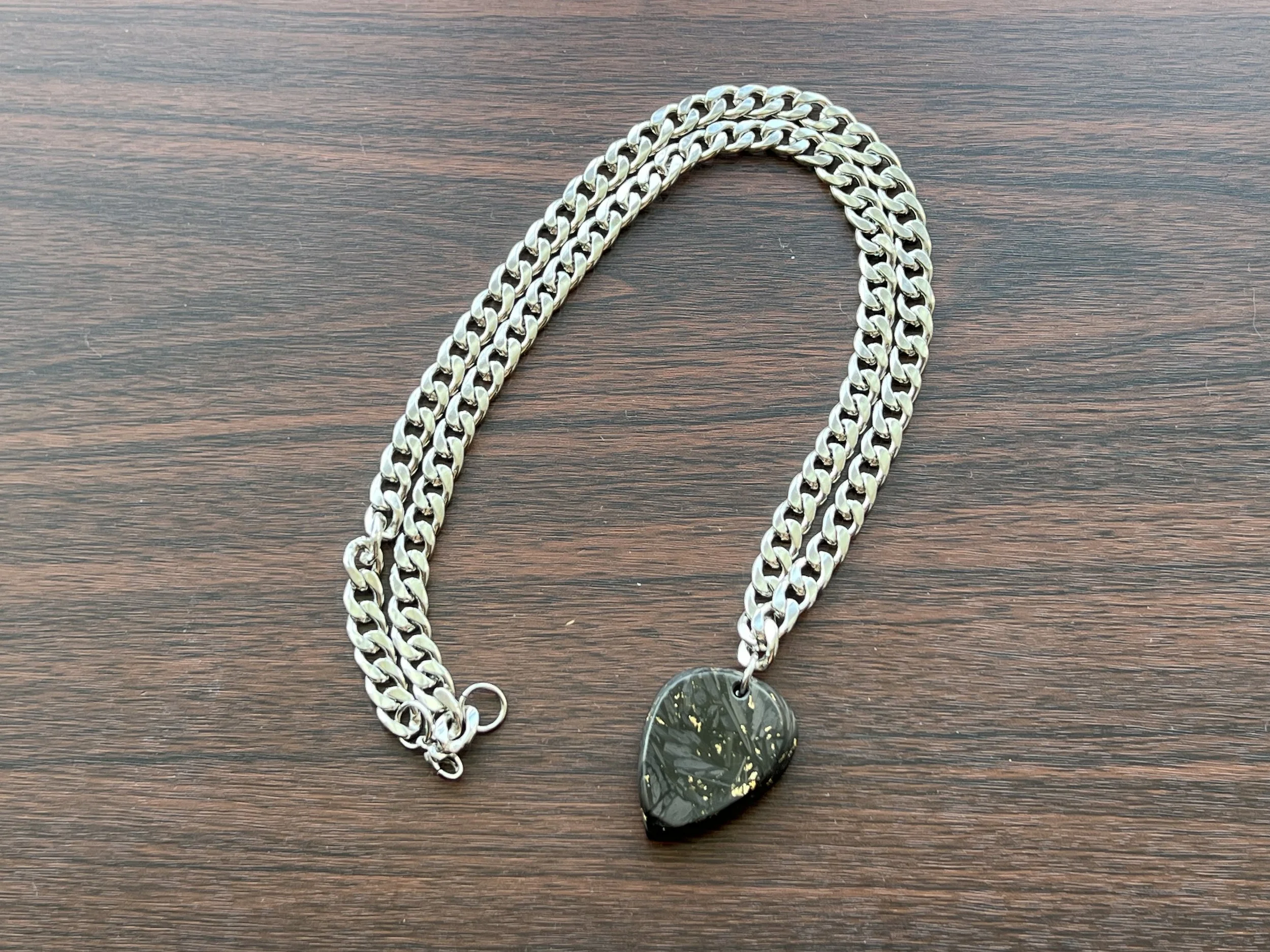 A silver chain necklace with a black and green pendant, lying on a wooden surface.