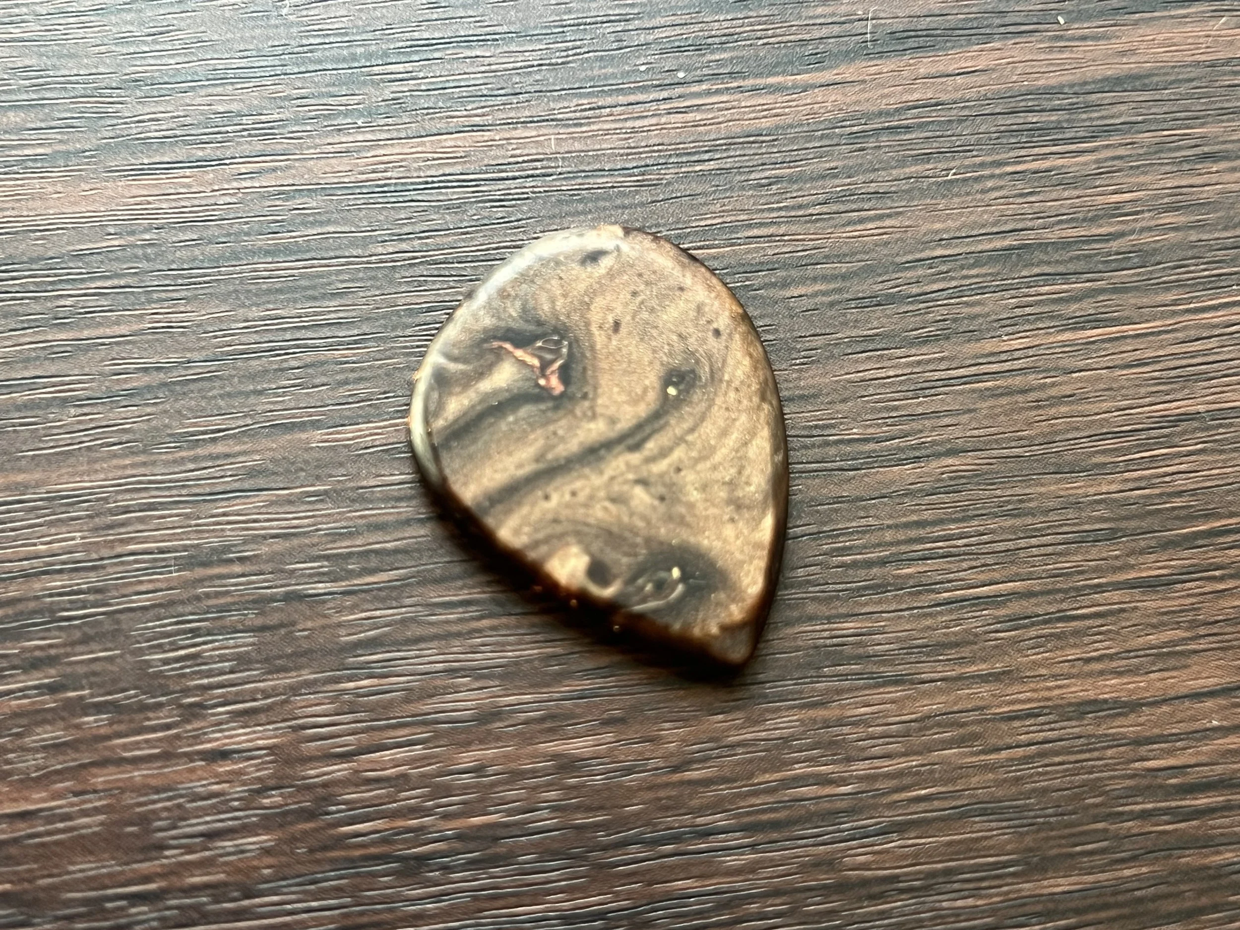 A close-up of a coin on a wooden surface, showing part of a person's face with light-colored hair.