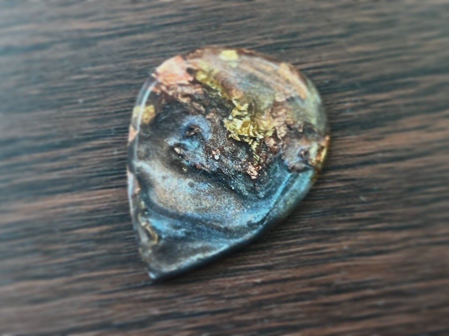 A close-up photograph of a melted, irregularly shaped piece of ice with embedded debris on a dark wooden surface.