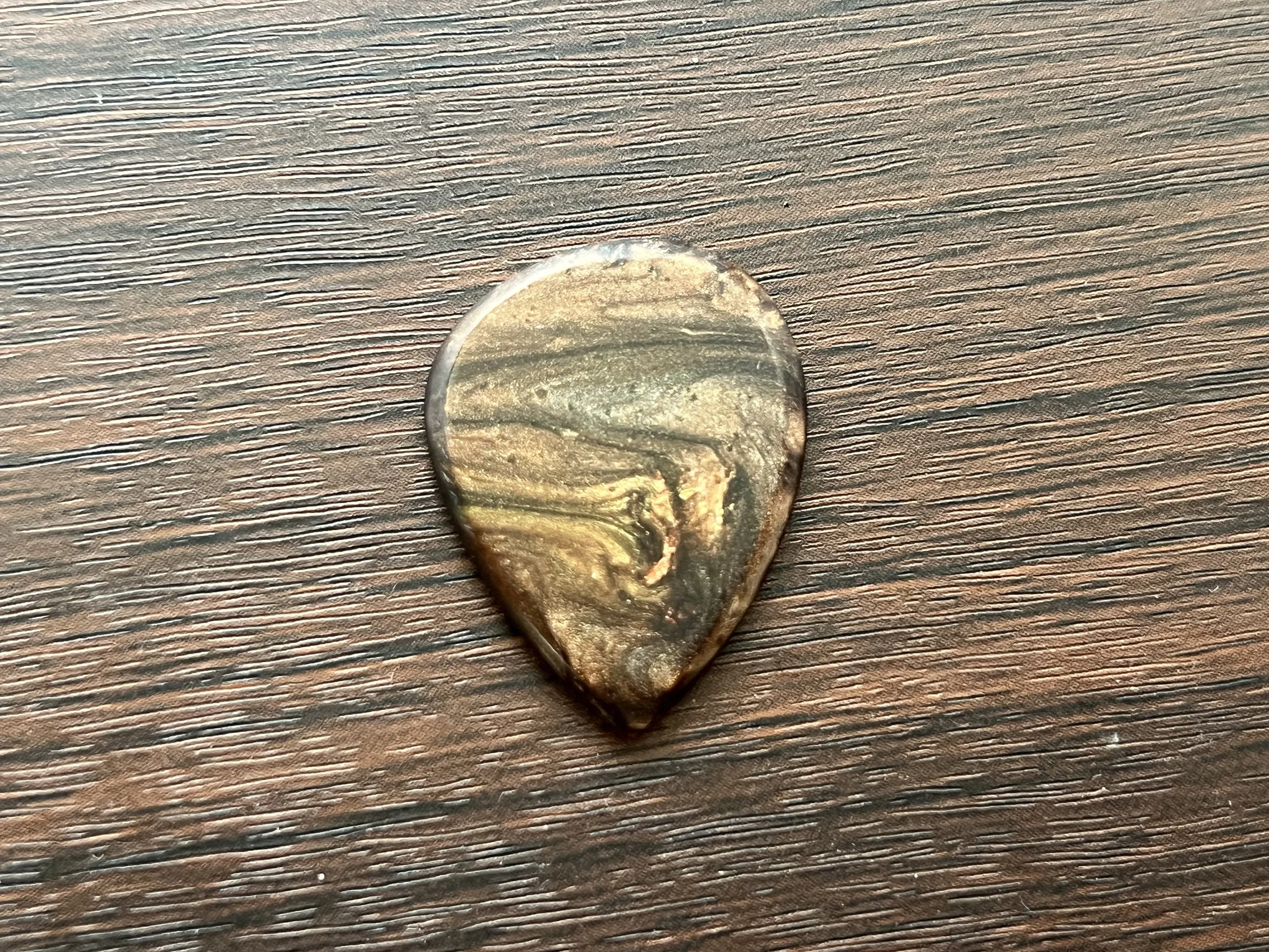 Close-up of a small, irregularly shaped, semi-translucent stone or mineral on a wooden surface with horizontal grain.