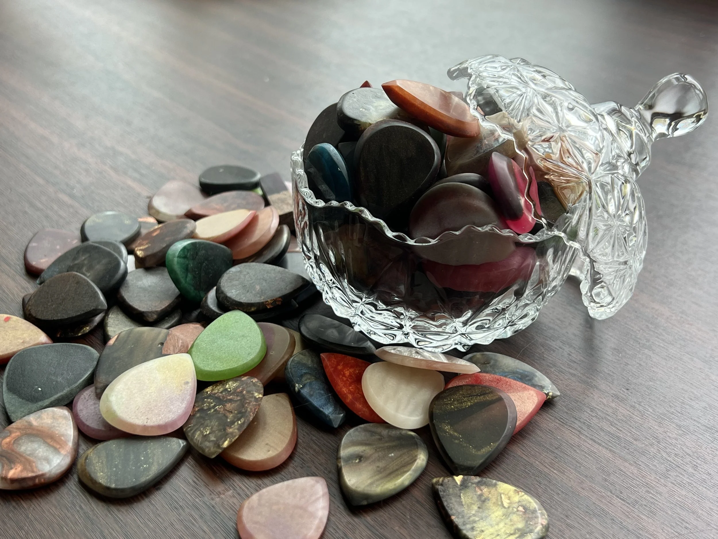 Colorful polished stones spilling out of a clear crystal dog-shaped container onto a wooden surface.