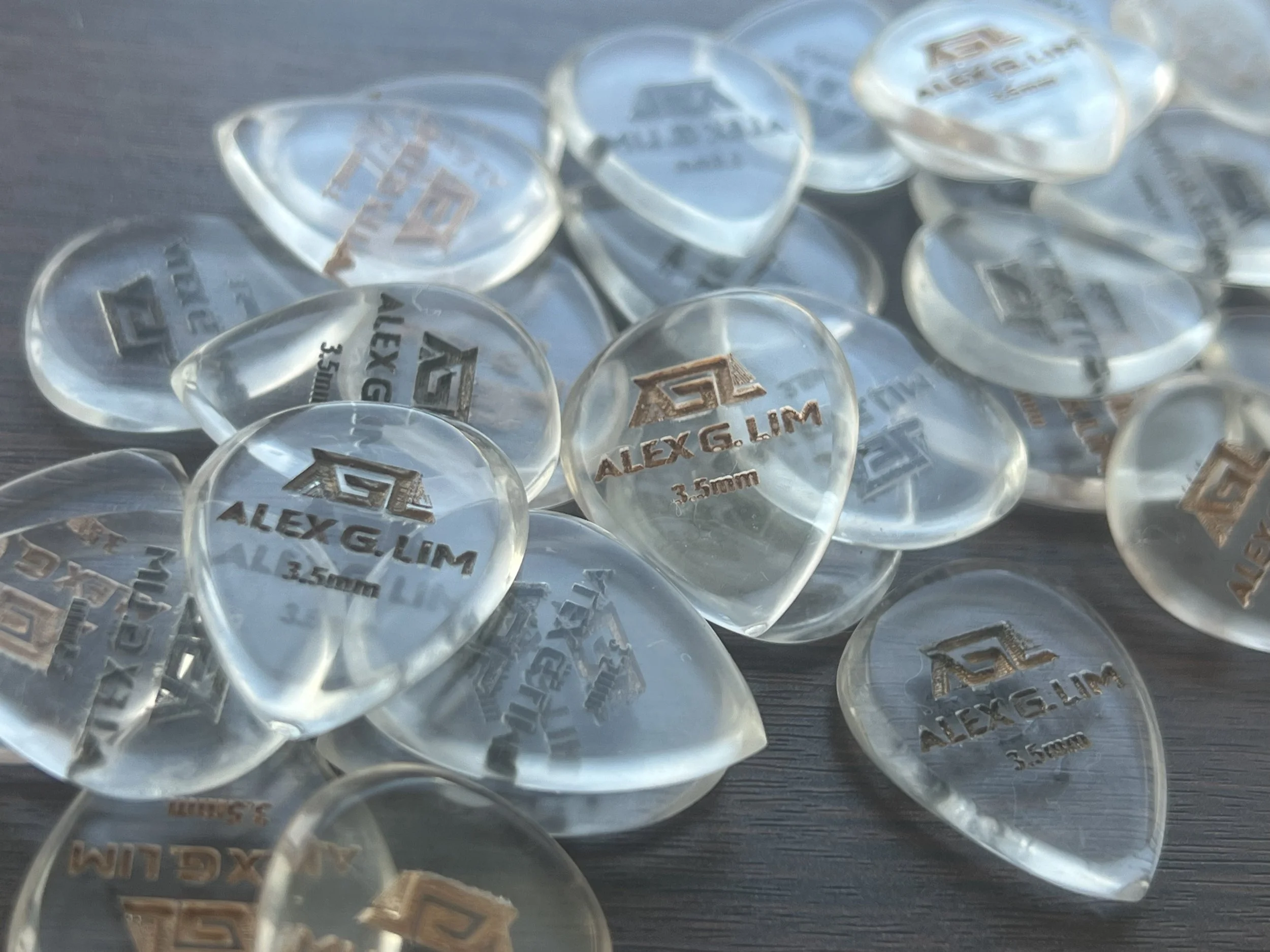 Close-up of multiple transparent dice with engraved text, including names and measurements, scattered on a dark wooden surface.
