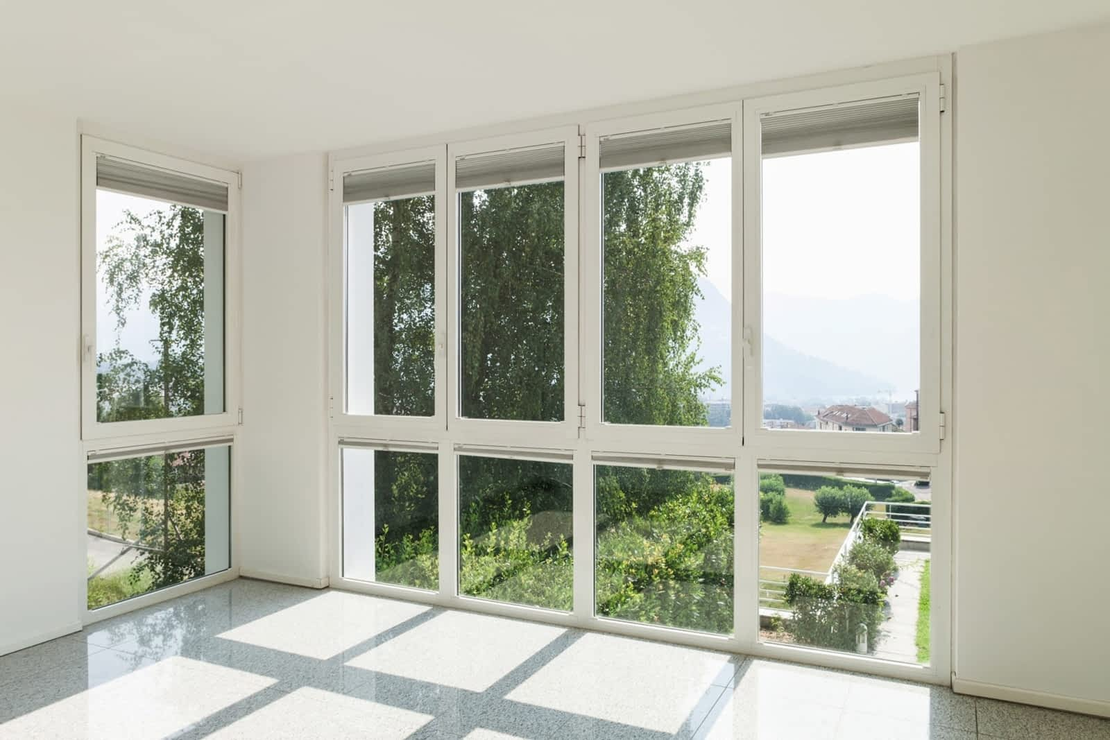 Empty room with large windows showing trees, houses, and mountains outside.