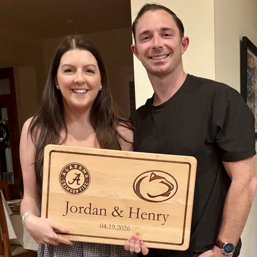 Couple holding a personalized wooden cutting board engraved with the names Jordan and Henry and their wedding date.