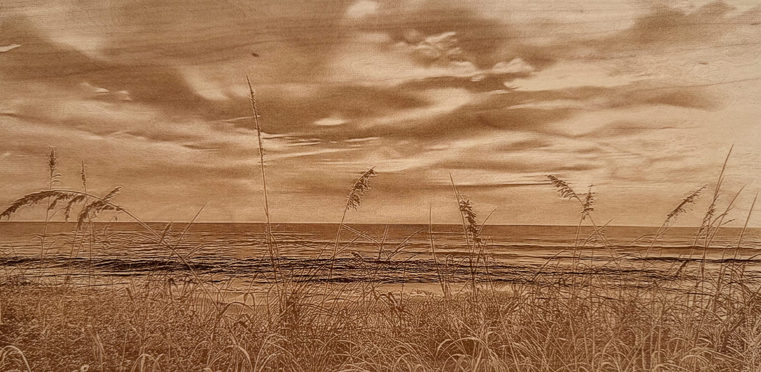 Laser-engraved hardwood landscape showing seagrass-covered dunes with the ocean in the background.