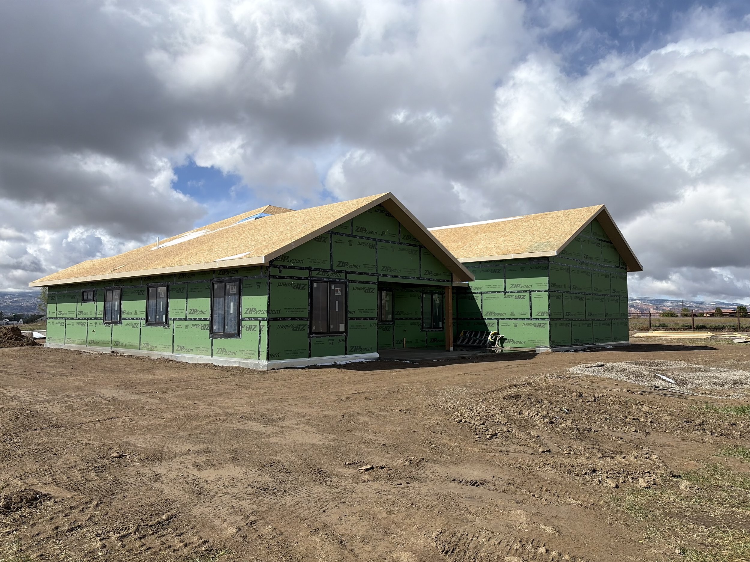 A house under construction with completed ZIP sheathing standing on a dirt lot with a cloudy sky overhead.