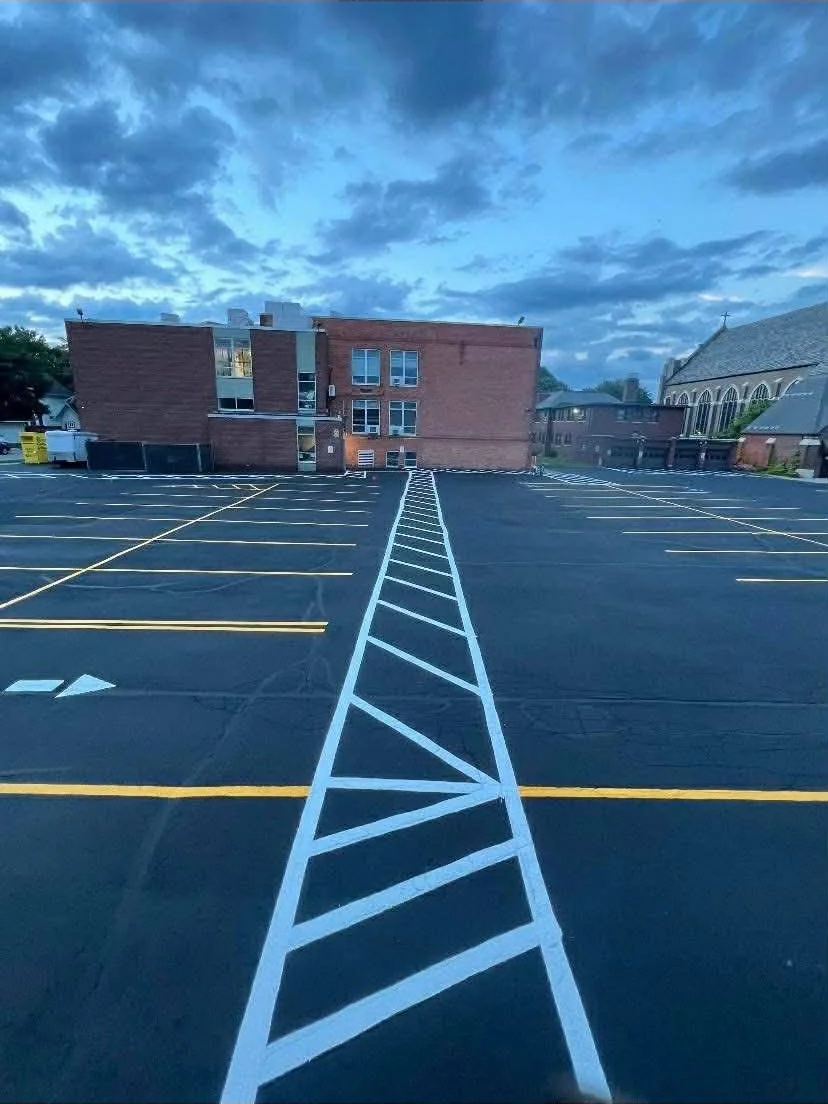 Empty parking lot with freshly painted lot lines and a brick building in the background under a cloudy sky.