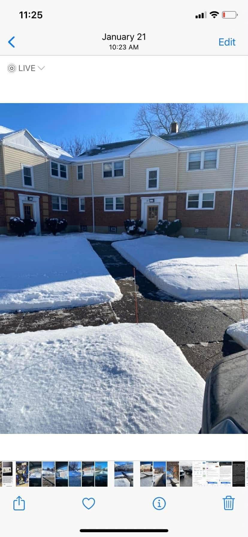 Snow-covered sidewalk and driveway in front of beige and brick residential building under clear blue sky.