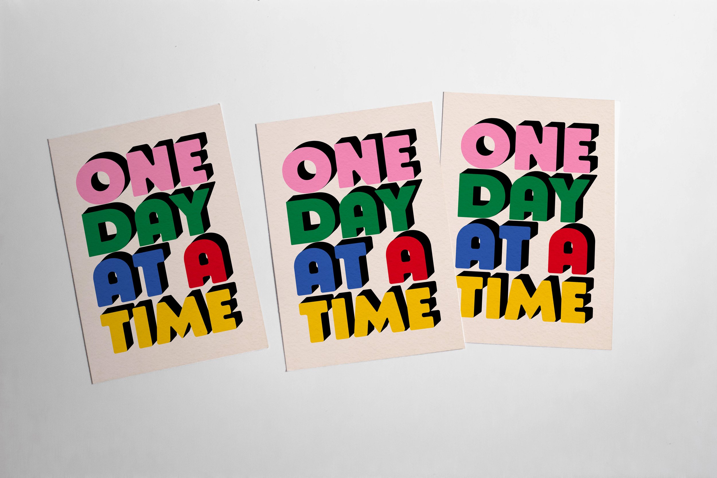 Three colorful posters with the phrase 'One day at a time' in bold, multicolored letters.