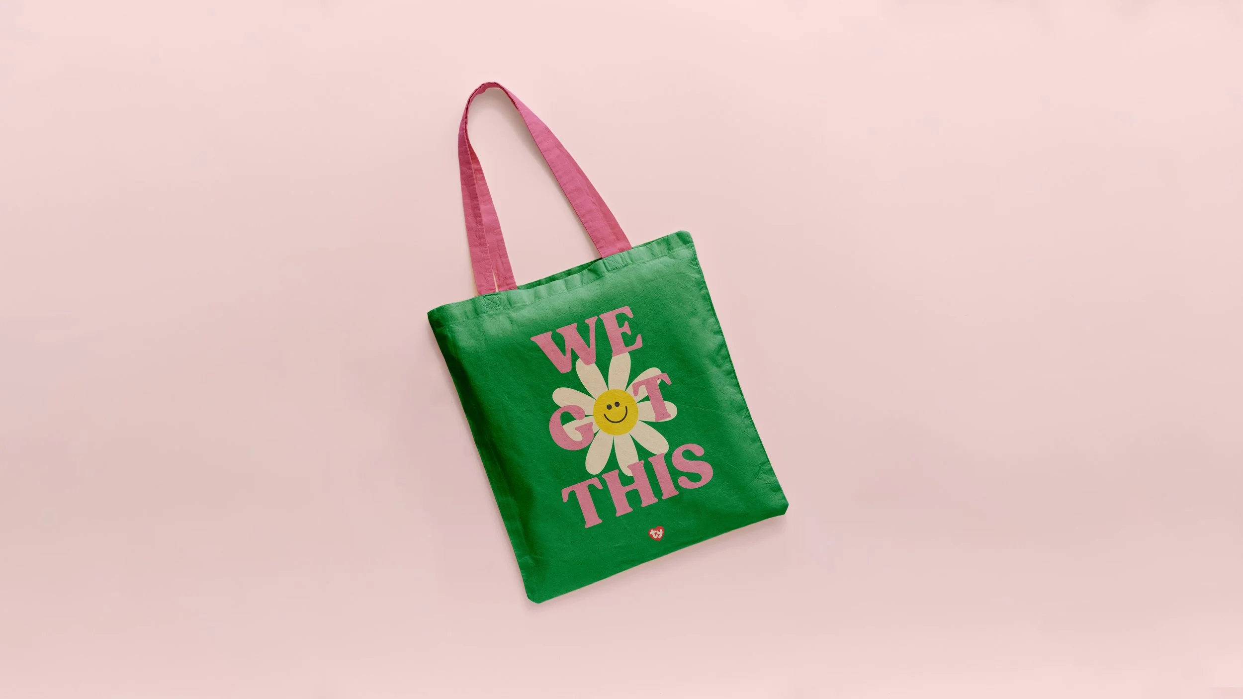 Green tote bag with pink handles and the words 'WE GOT THIS' in pink letters, featuring a smiling daisy with a yellow face on a pink background.