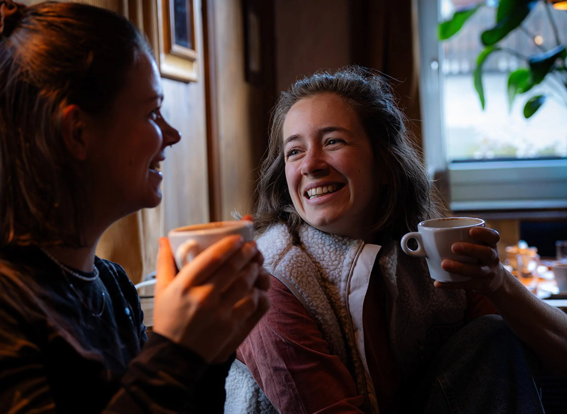 Zwei lachende Frauen sitzen in einem Café und trinken Kaffee.