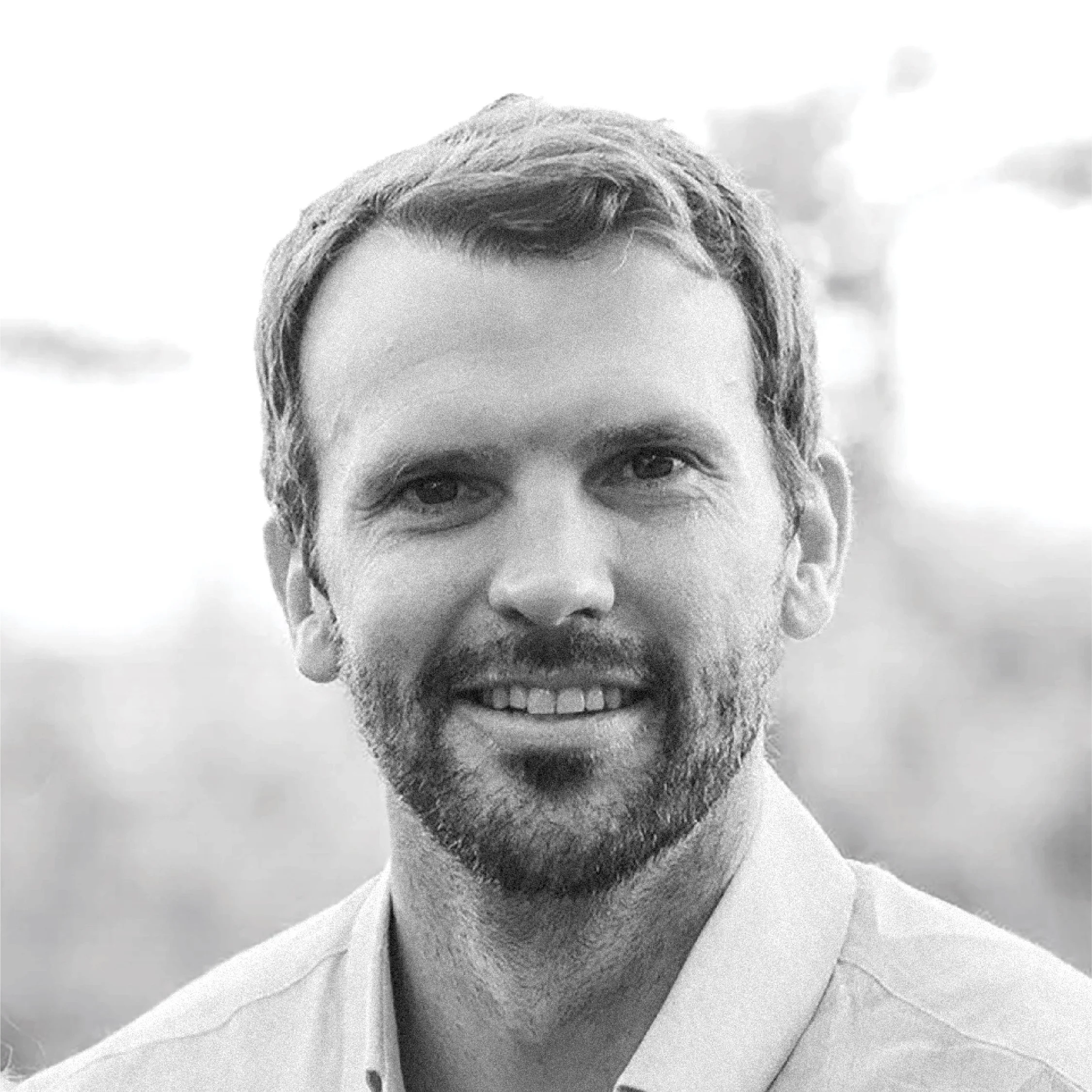 Black and white close-up of a smiling man with short hair, beard, and wearing a collared shirt.