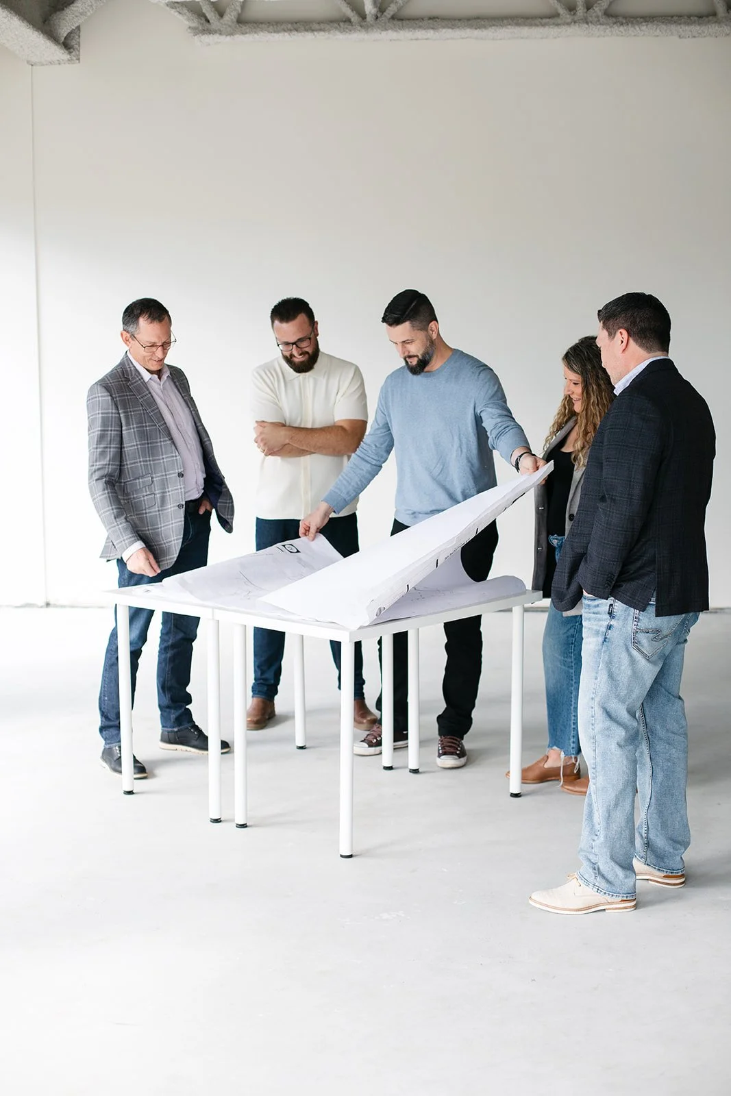 Group of five people, PRAXA Projects team, gathered around a table looking at plans or blueprints in a bright, minimalistic space.