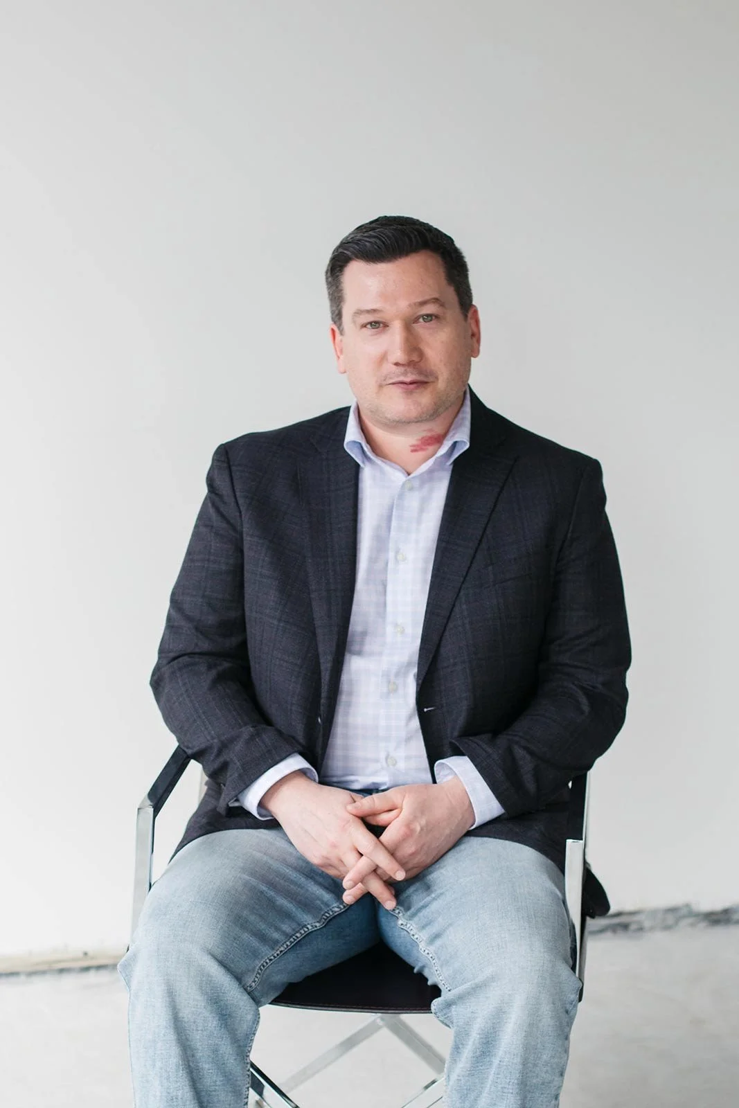 Jared Riehl, Vice President, Finance V2CM, in a dark suit and shirt standing in front of a wooden wall, smiling.