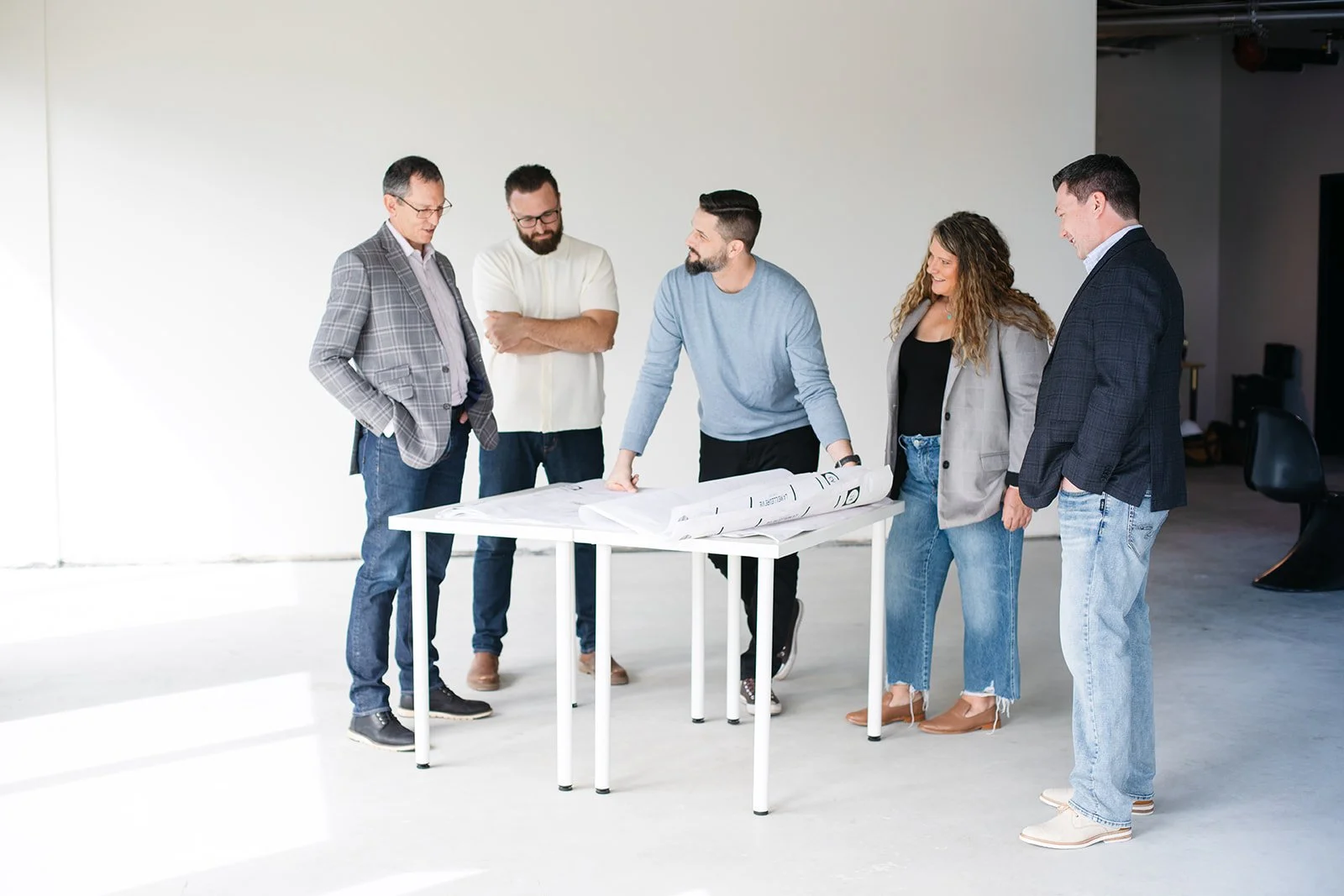 Praxa Projects Team, Group of five people discussing in a modern, minimalistic room with architectural plans on a white table.
