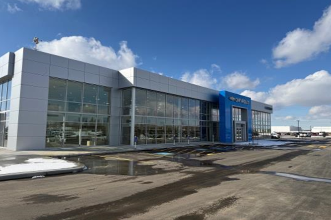 Exterior view of a modern Chevrolet car dealership building with large glass windows and a blue Chevrolet sign, on a partly cloudy day.