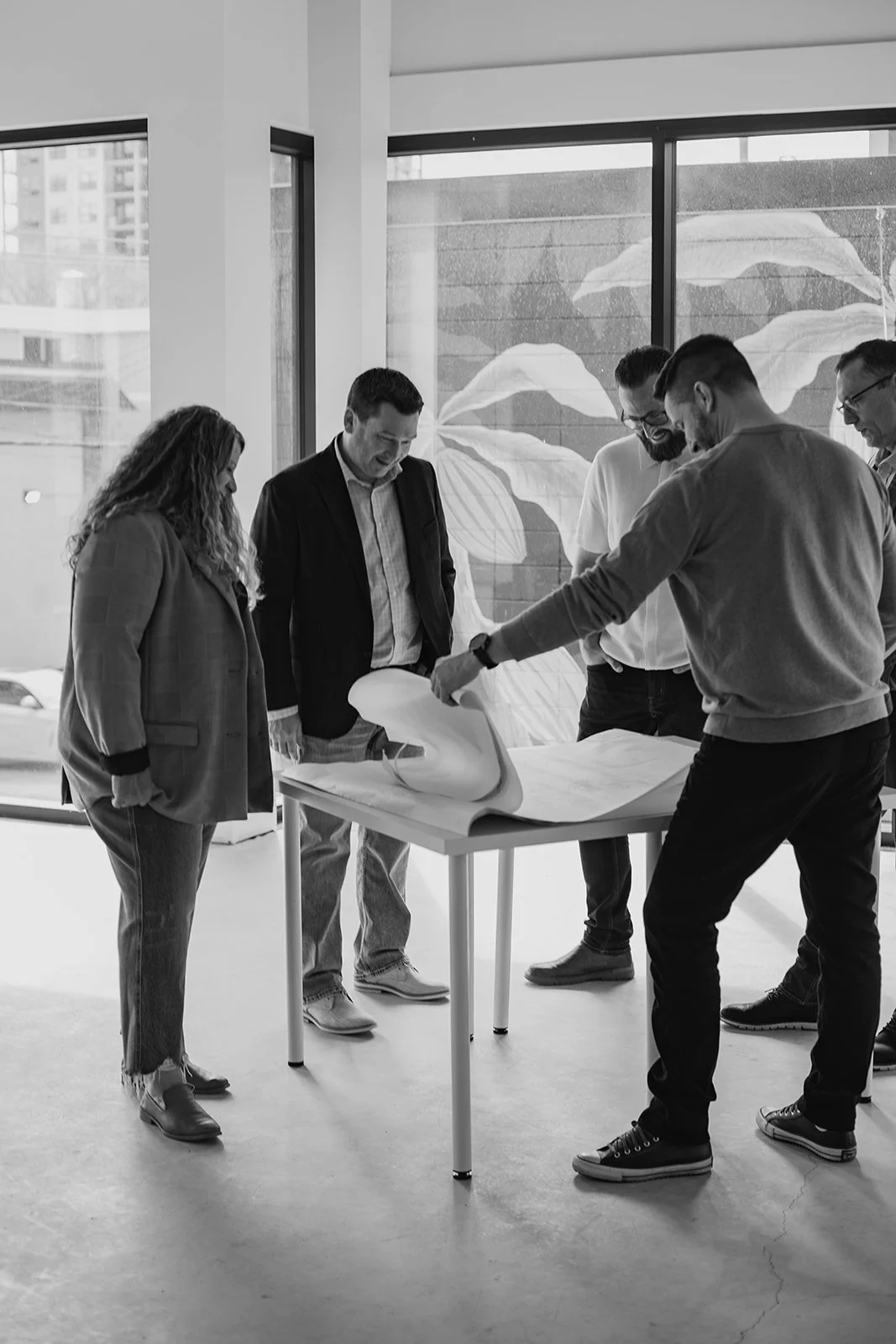 Praxa Projects Team, Five people in a modern office, gathered around a table reviewing large architectural plans.
