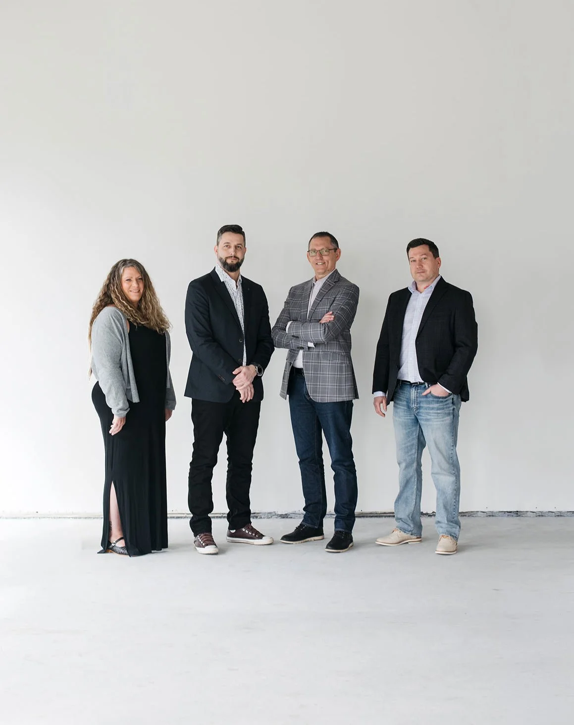 Group of four people standing together in a minimal white room, dressed in business casual attire.