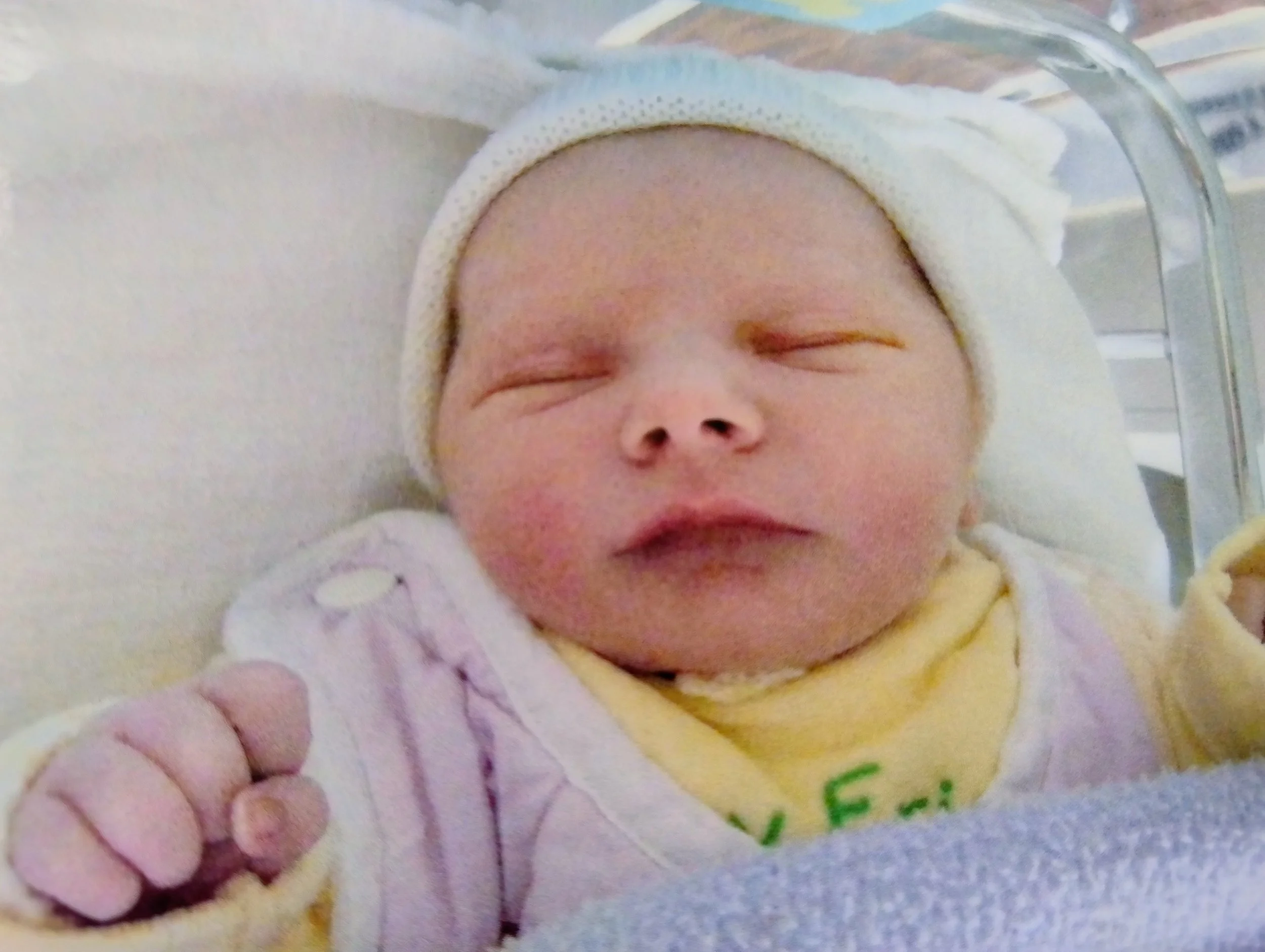 Bébé endormi dans un lit d'hôpital, portant un chapeau blanc et une tenue jaune.