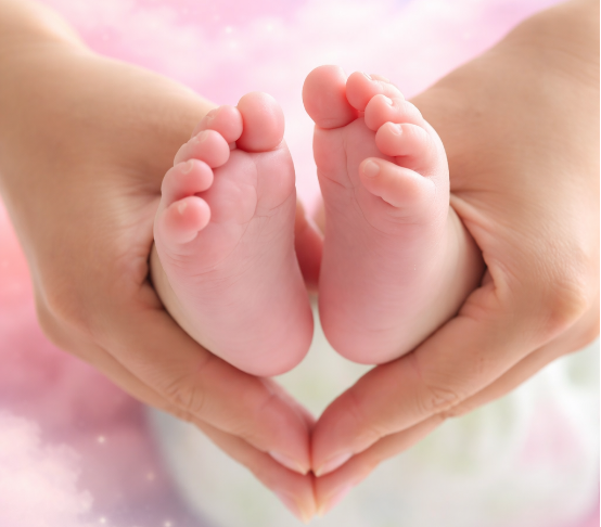 Une main adulte tenant délicatement deux petits pieds de bébé formant un cœur.