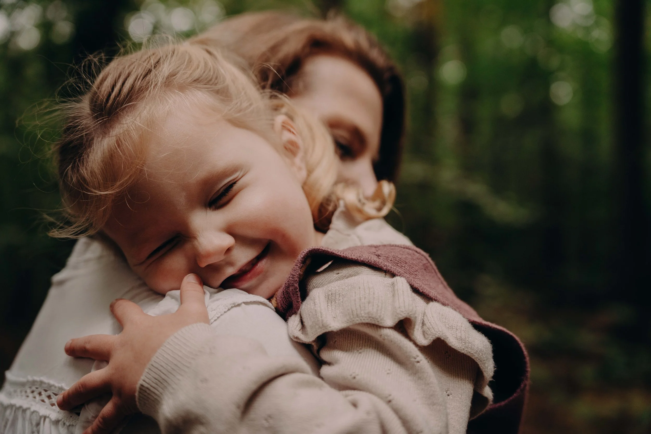 Foto van een moeder en klein meisje die knuffelen in het bos