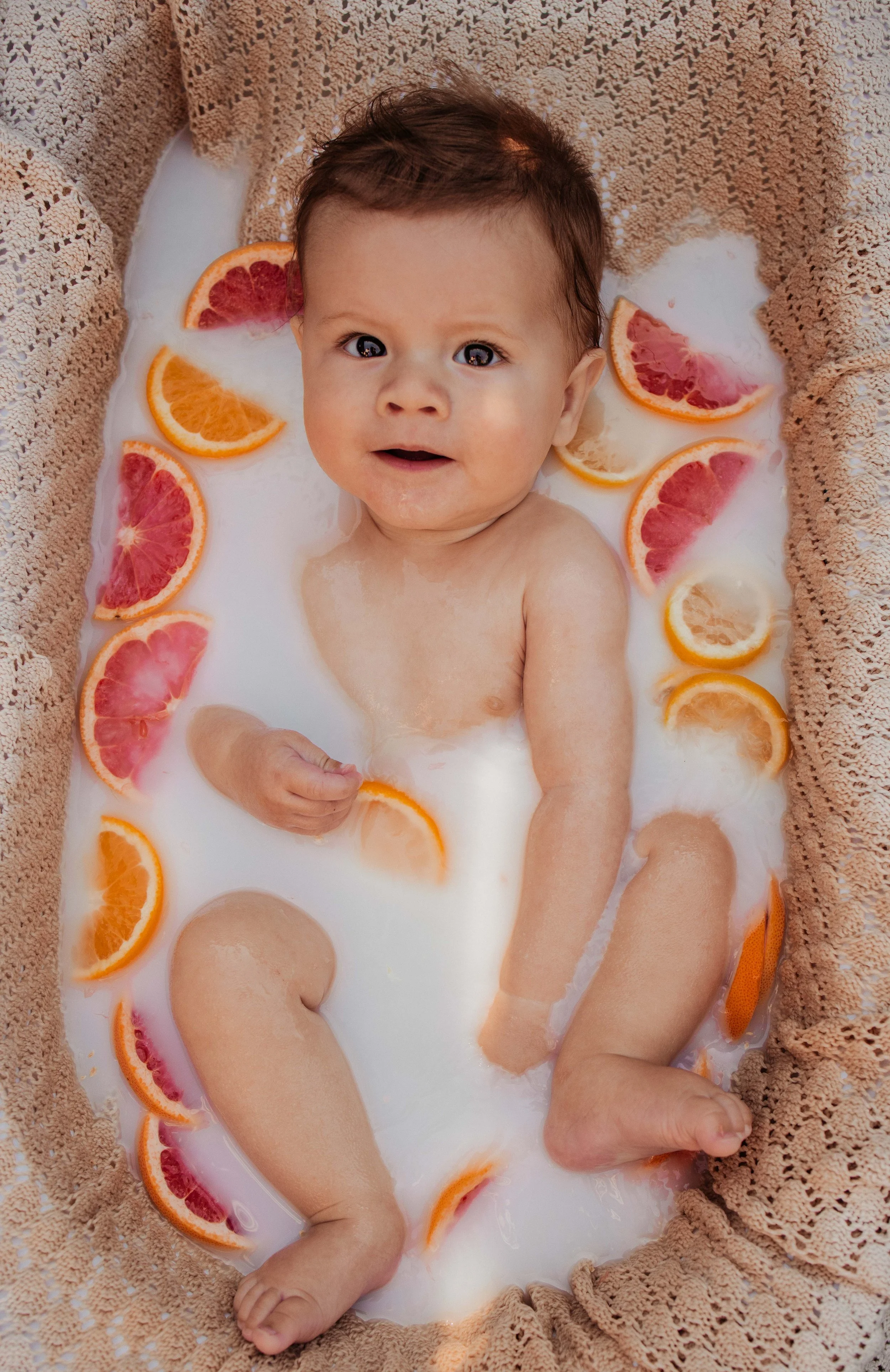 Foto van een baby in een melkbad met citrusvruchten
