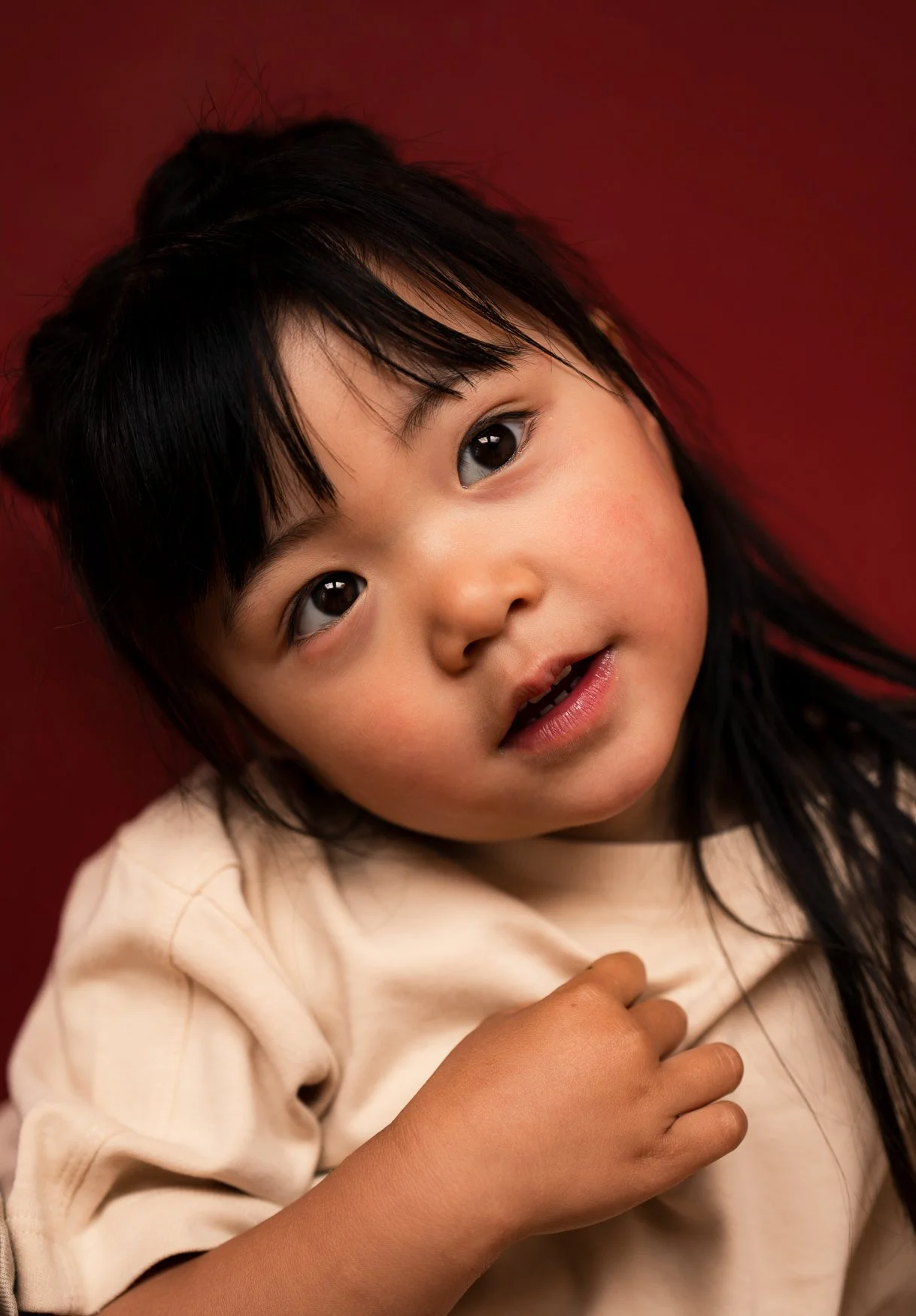 Portret van een jong meisje met lange donkere haar, liggend op een rood achtergrond, naar de camera kijkend.