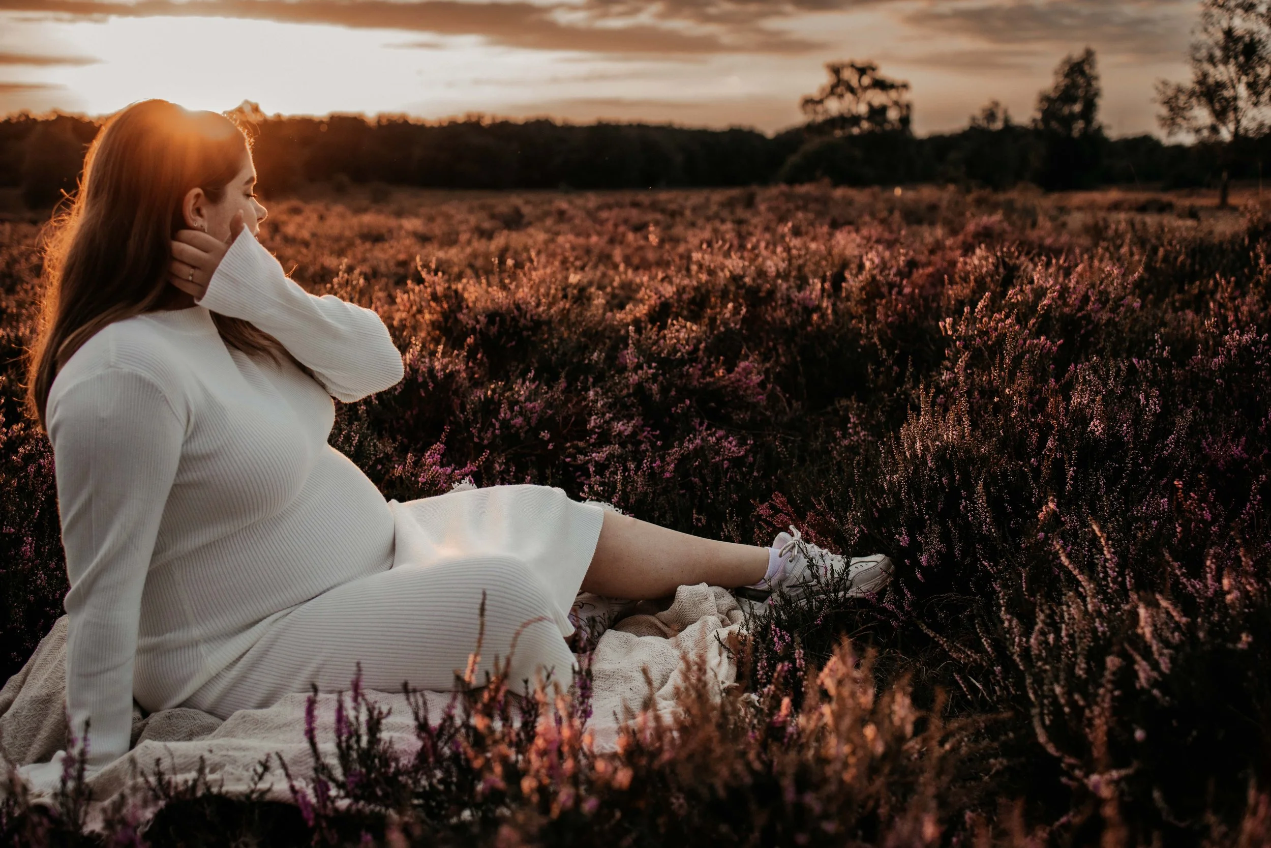 Foto van een jonge zwangere vrouw in de bloeiende heide tijdens het gouden uurtje