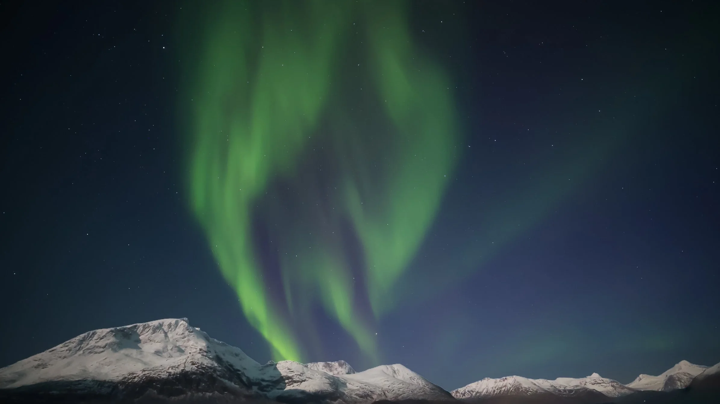 Northern lights illuminating a night sky over snow-covered mountains.