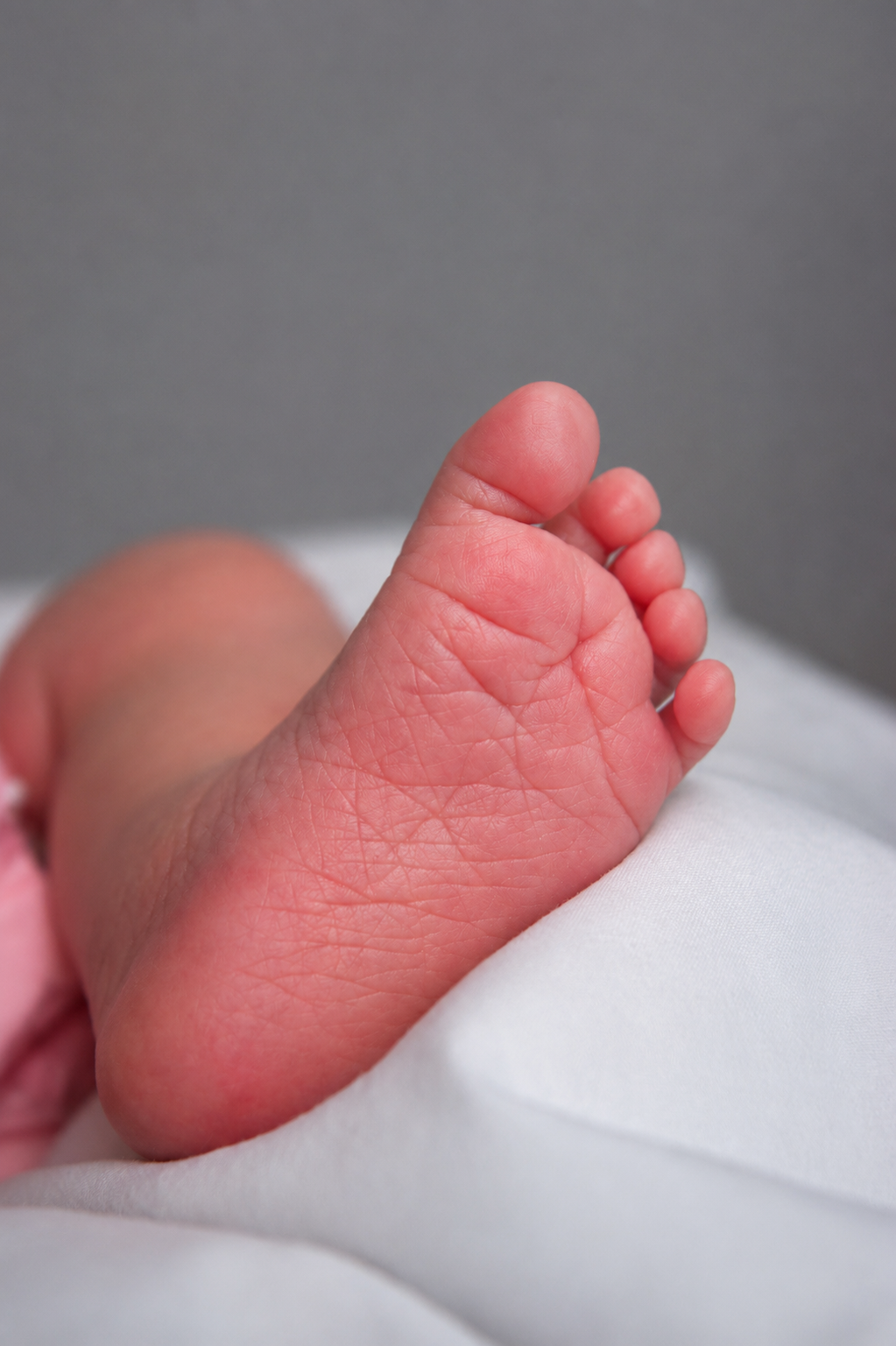 Close-up of a newborn baby's foot with tiny toes resting on a white blanket.