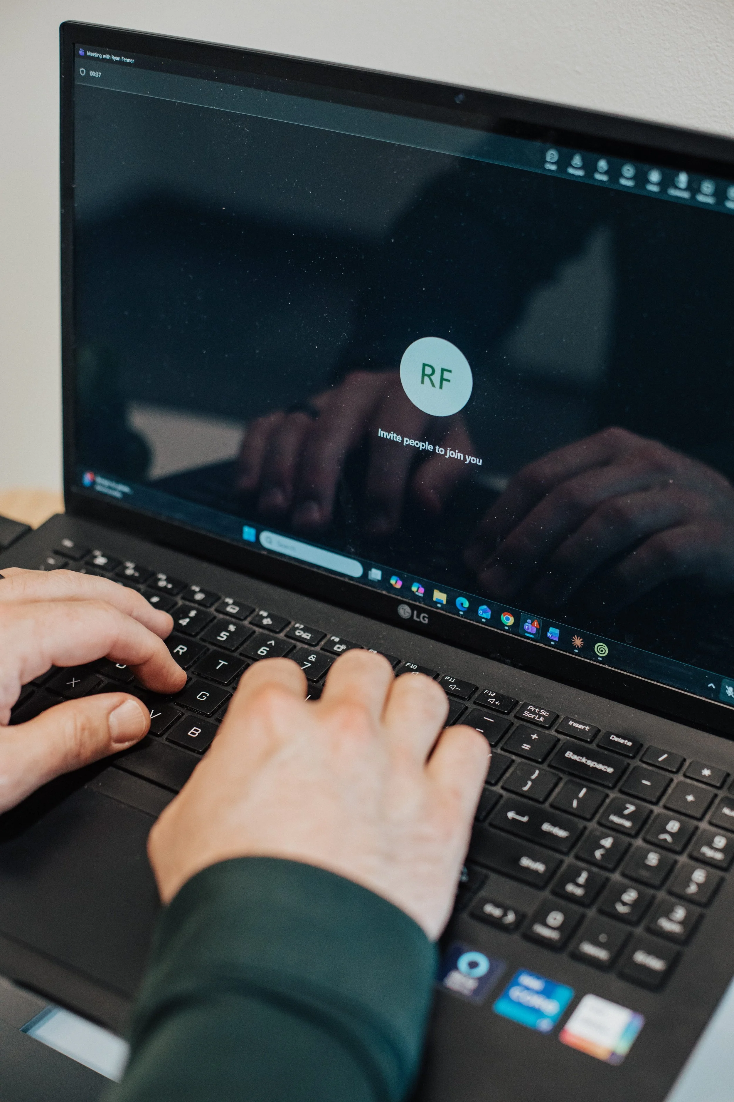 Close-up of person typing on a black laptop keyboard, with a video call screen visible on the monitor showing a blank circle with initials 'RF' and the text 'Invite people to join you.'