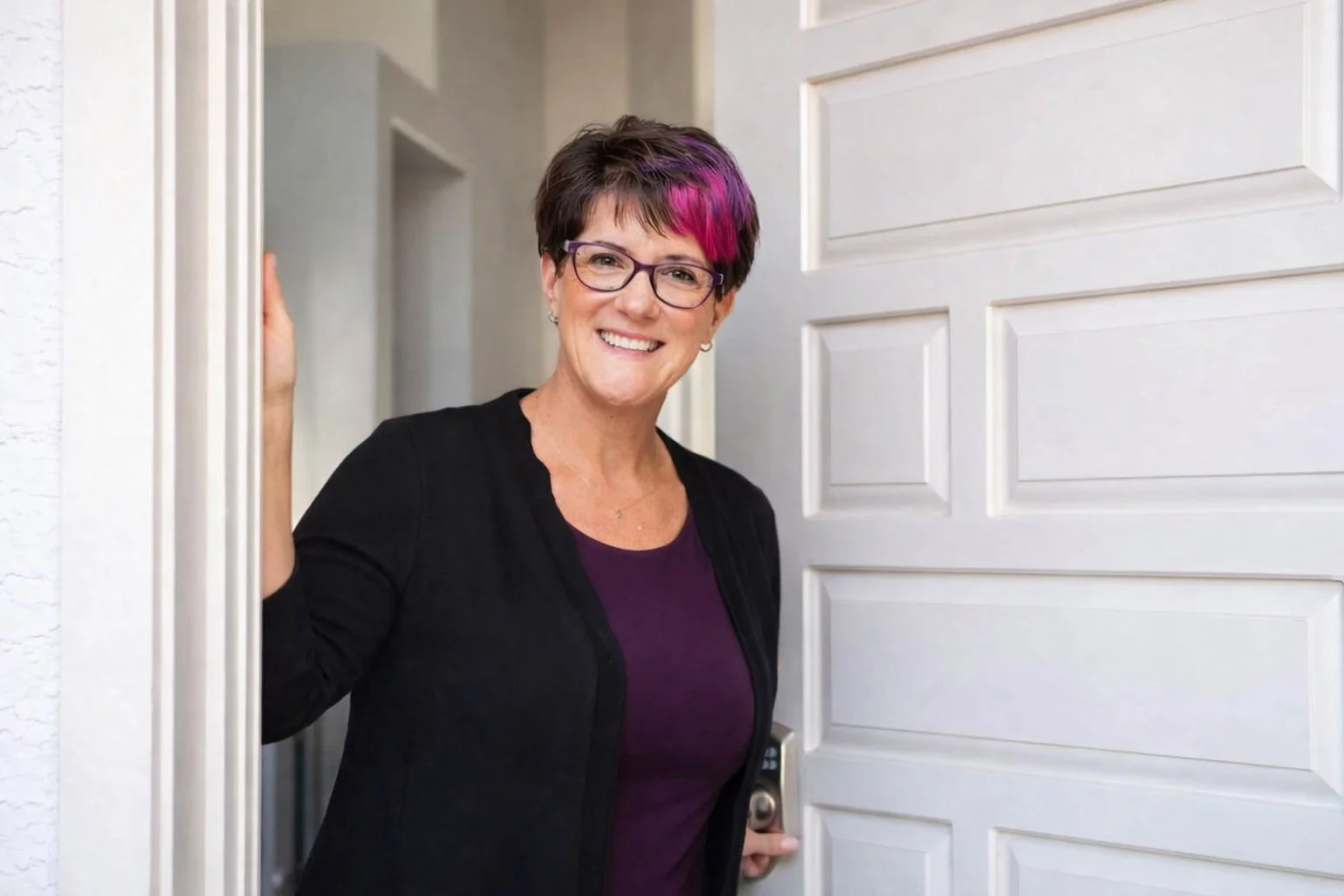 Picture of Susan Gregory standing inside of a door frame smiling with her hand resting on the door frame.