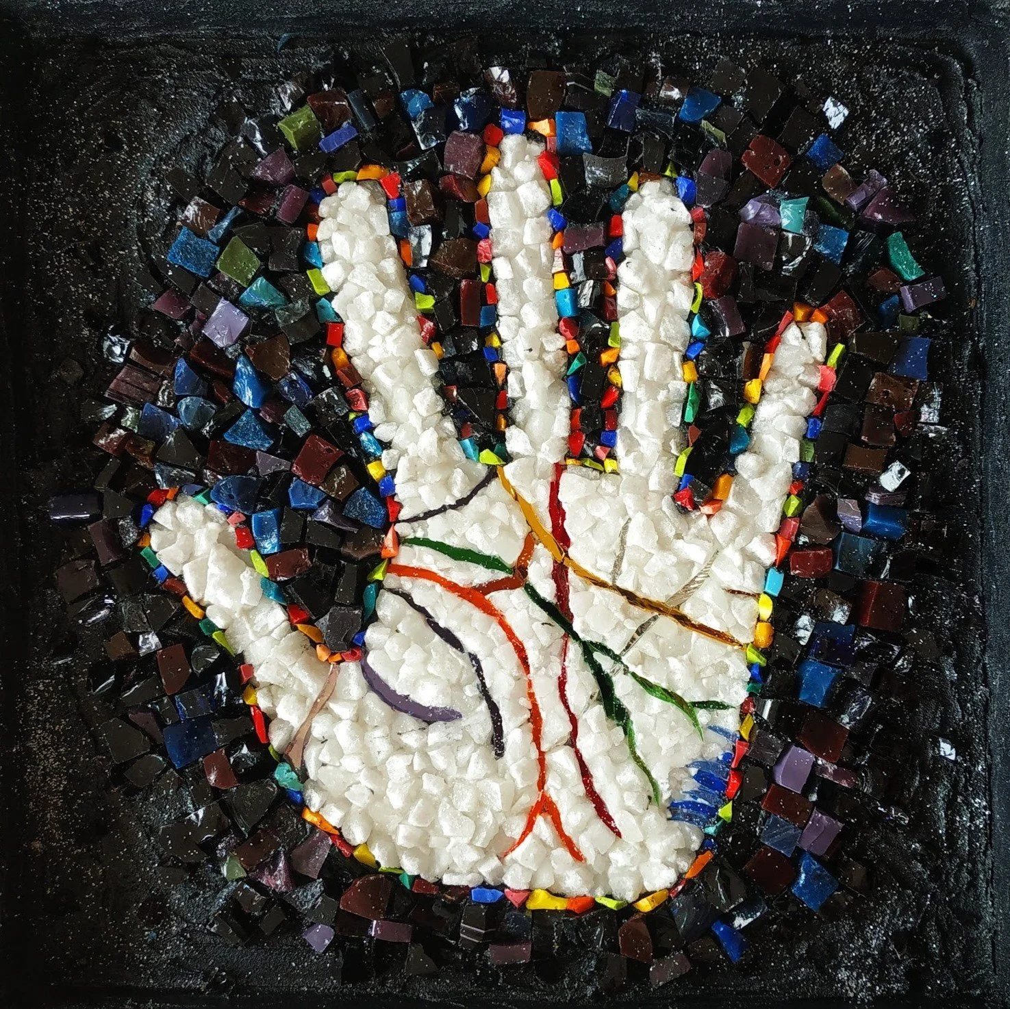 Mosaïque d'une main stylisée avec des fils multicolores à l'intérieur, entourée de petits cubes de verre noir, bleus, verts, rouges, jaunes, violets, formant un fond dense. L'ensemble est en mosaïque colorée.