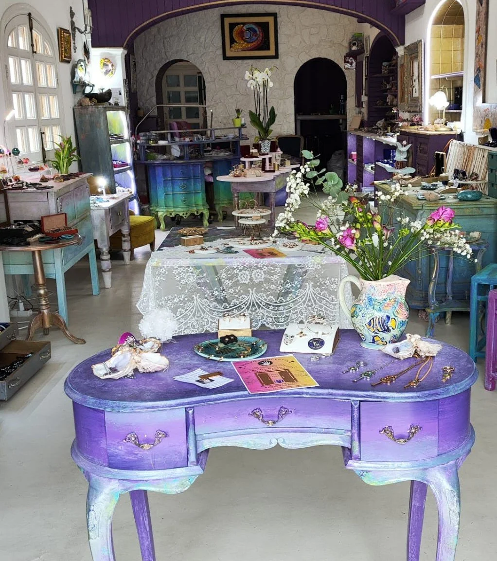 Une boutique d'antiquités ou de décoration intérieure, avec diverses meubles colorés, bijoux et objets décoratifs, et un vase avec des fleurs dans le centre.