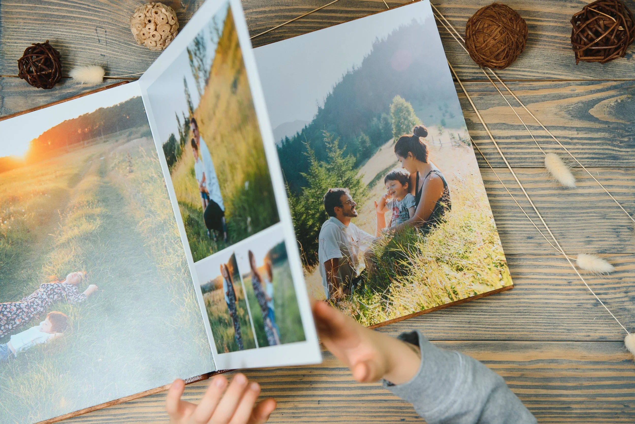 A person flipping through a photo album with outdoor pictures of a family enjoying nature, sitting on a wooden surface decorated with dried decorative balls and plants.